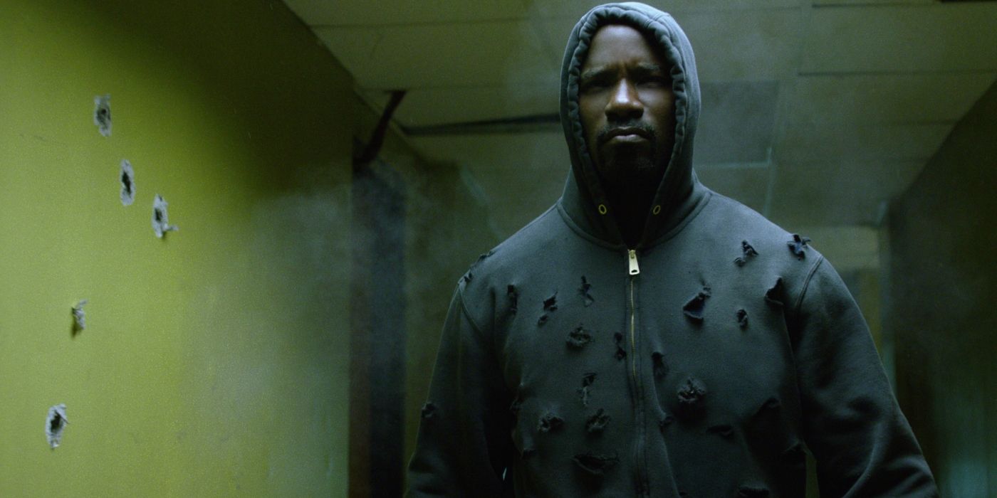 Luke Cage walks down a hallway, wearing a sweatshirt riddled with bullet holes