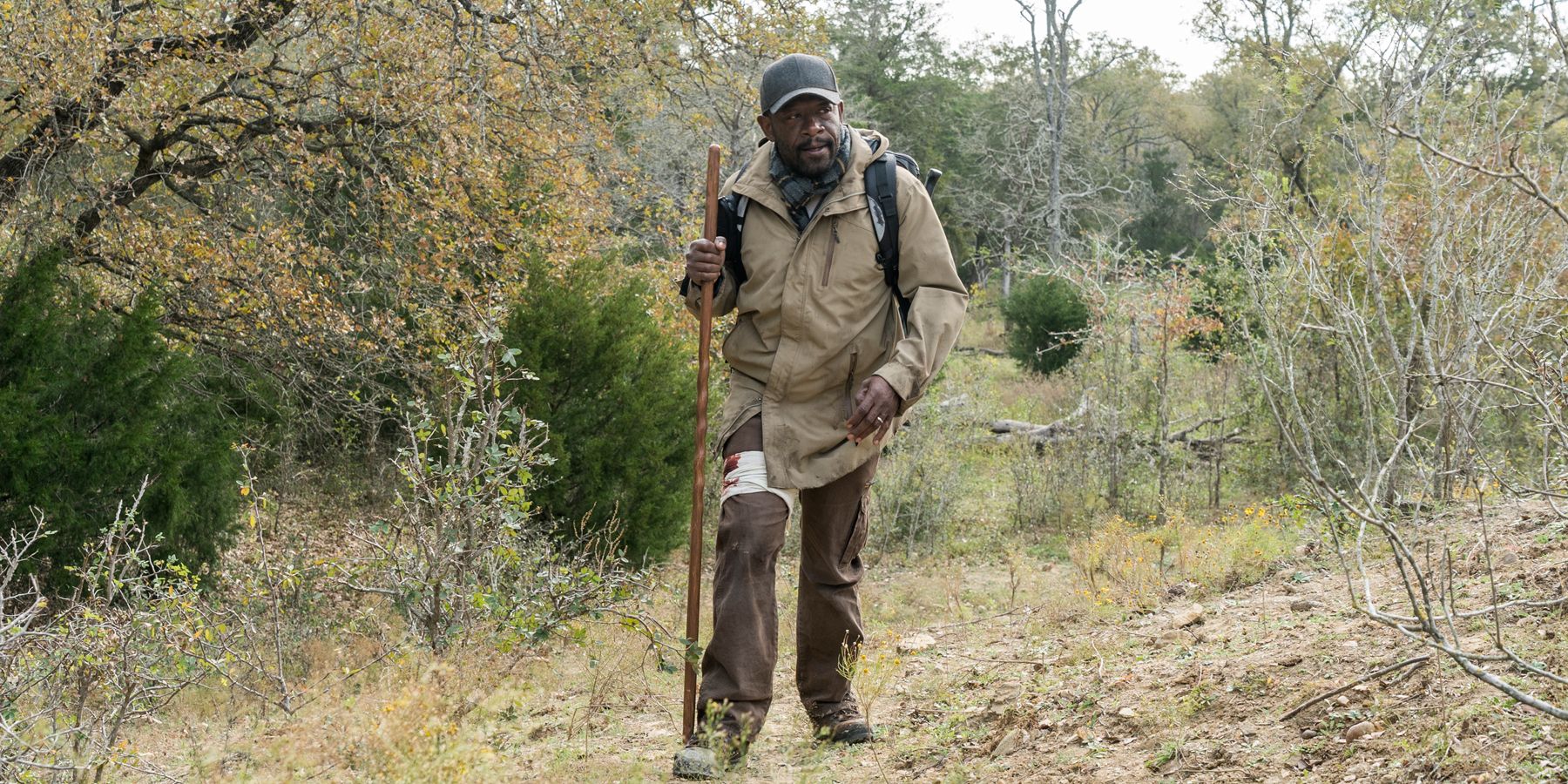 Morgan from The Walking Dead standing with a stick and a backpack.