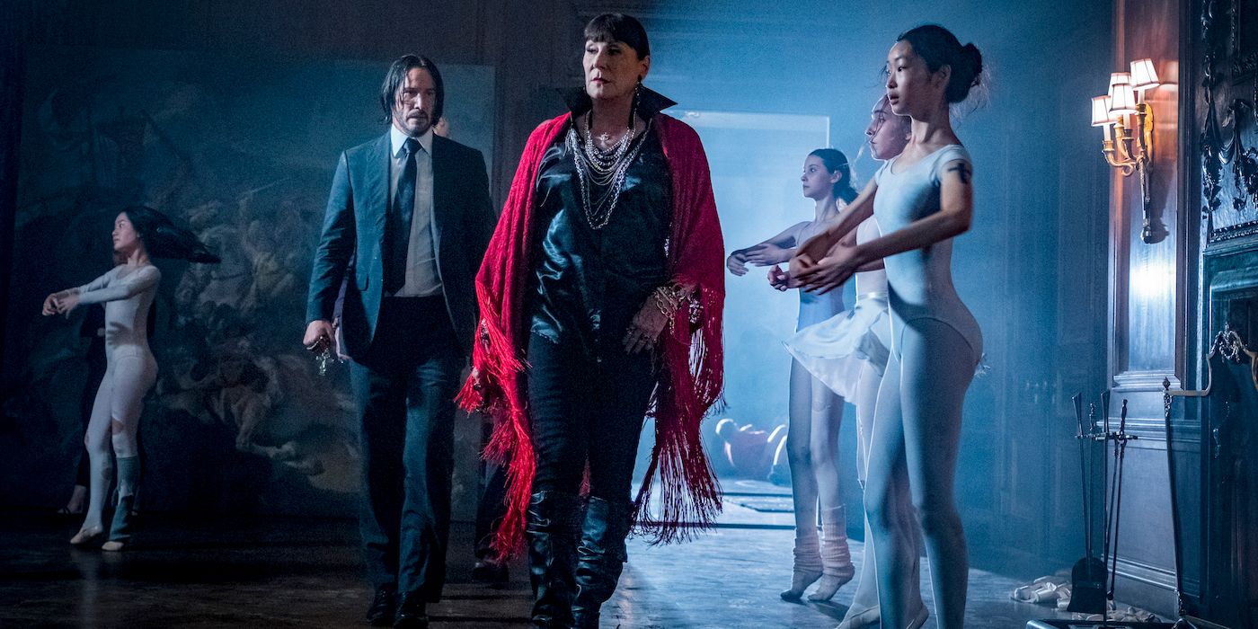 Anjelica Huston as the Director walks with Keanu Reeves' John Wick in front of ballerinas