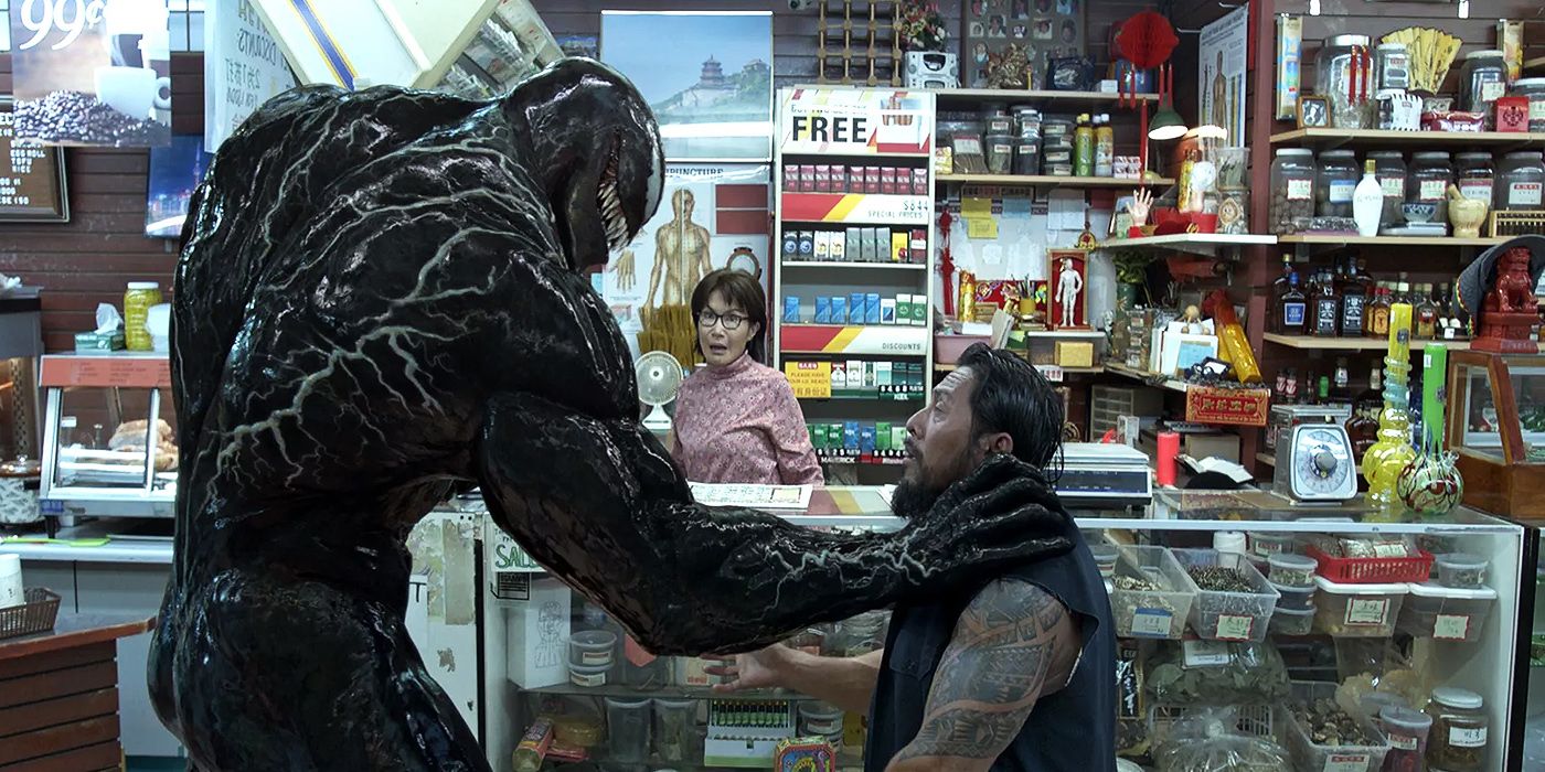 Venom grabs a robber by the throat in front of Mrs. Chen in Venom: Let There Be Carnage.