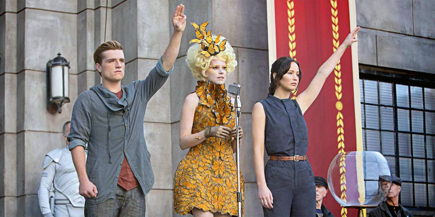 Katniss Everdeen e Peeta Mellark, dos Jogos Vorazes, cumprimentam ao lado de Effie Trinket