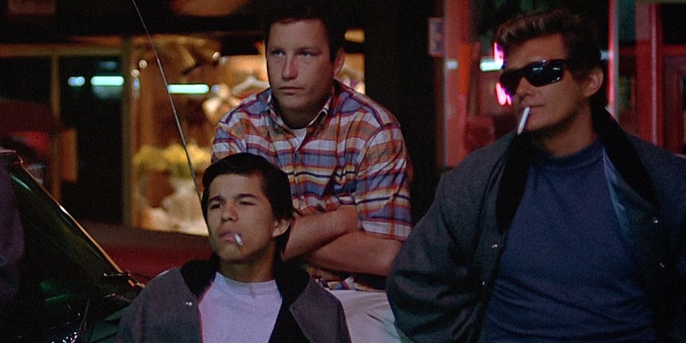 Um grupo de adolescentes encostado em um carro fumando cigarros em American Graffiti.