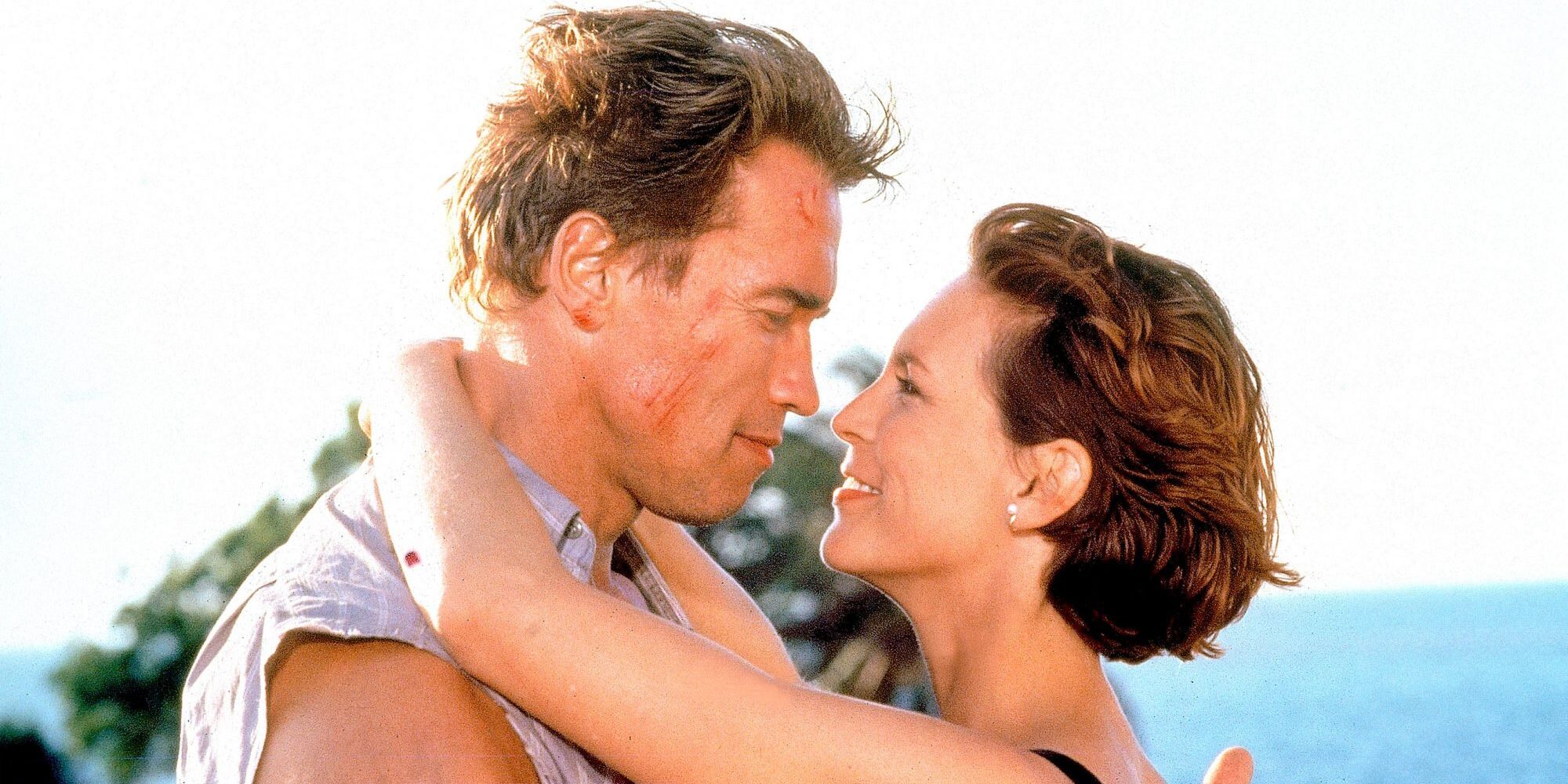 Arnold Schwarzenegger and Jamie Lee Curtis embrace each other on the beach in True Lies