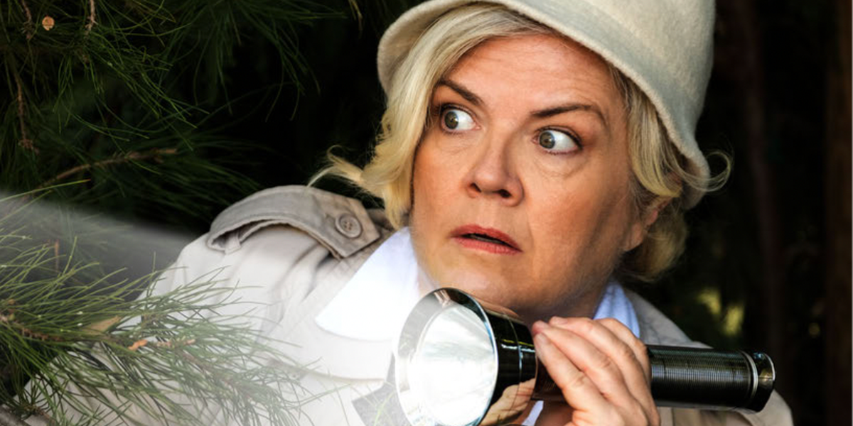 Paula Pell shines a flashlight while wearing a detective get-up.