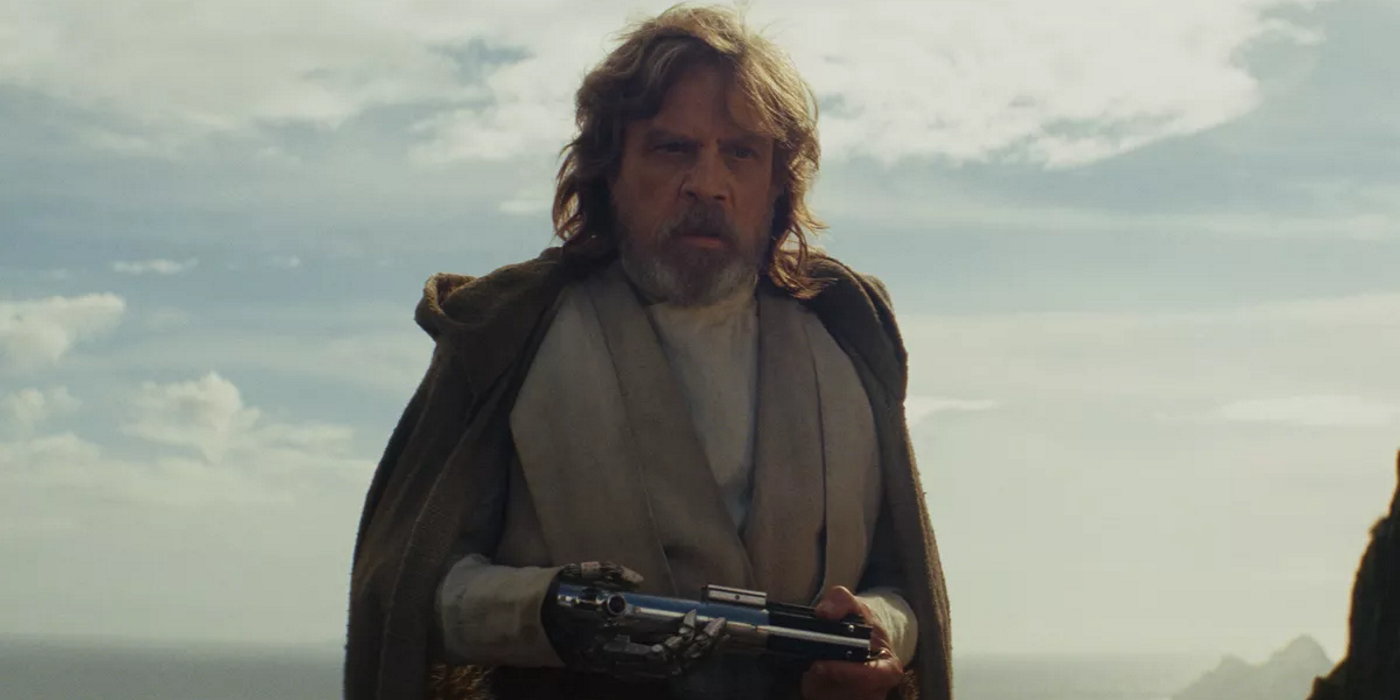 An older Luke Skywalker holding his lightsaber in his hands