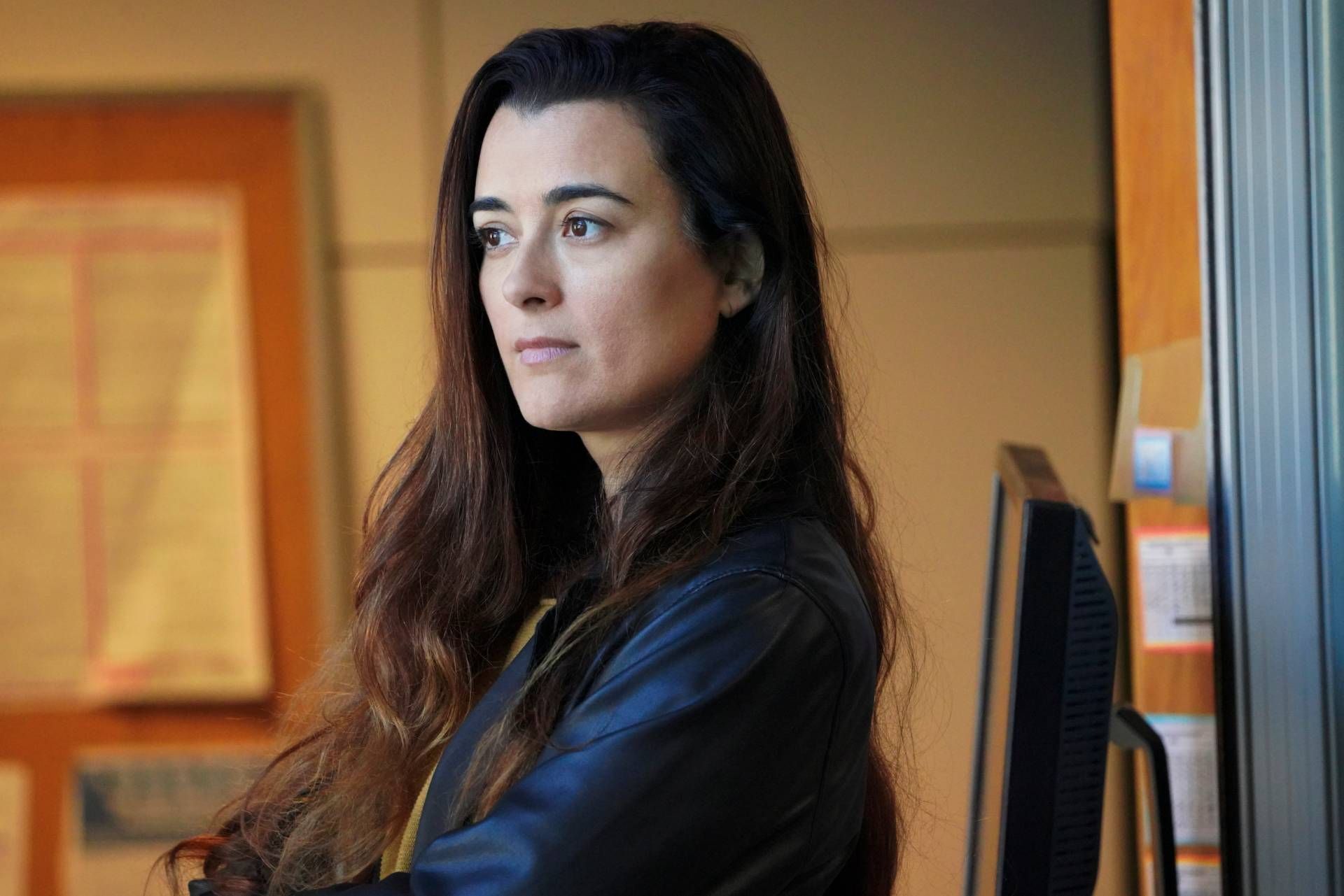 Ziva do NCIS está parada em um escritório com os braços cruzados