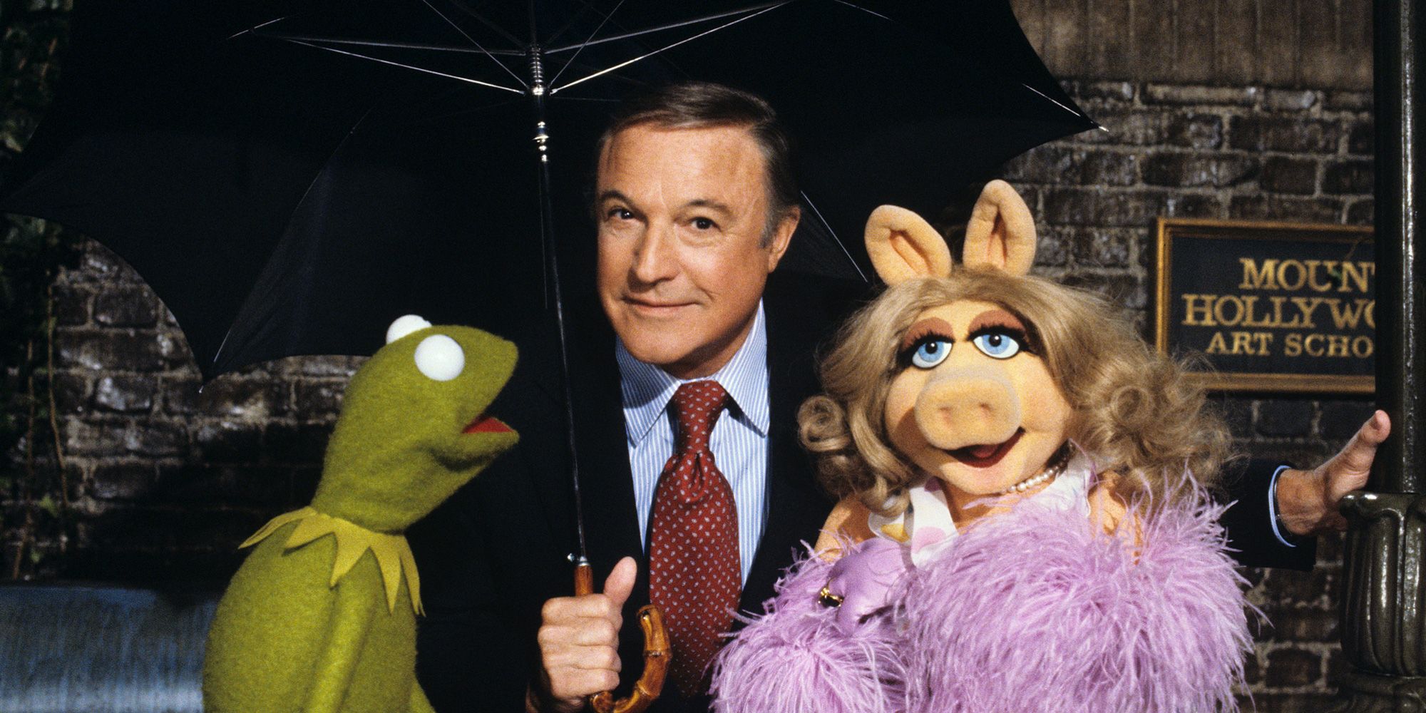 Actor Gene Kelly holding an umbrella and posing with Kermit the Frog and Miss Piggy