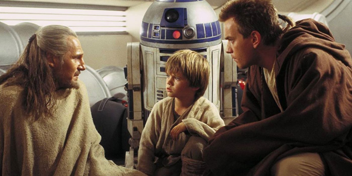 Qui-Gon Jinn speaking with young Anakin Skywalker while R2-D2 and Obi-Wan look on.