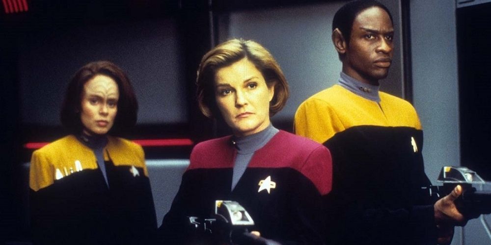 Voyager's Captain Janeway (played by Kate Mulgrew) holds a phaser rifle alongside Tuvok (Tim Russ) with B'Elanna Torres (Roxann Dawson) in the background