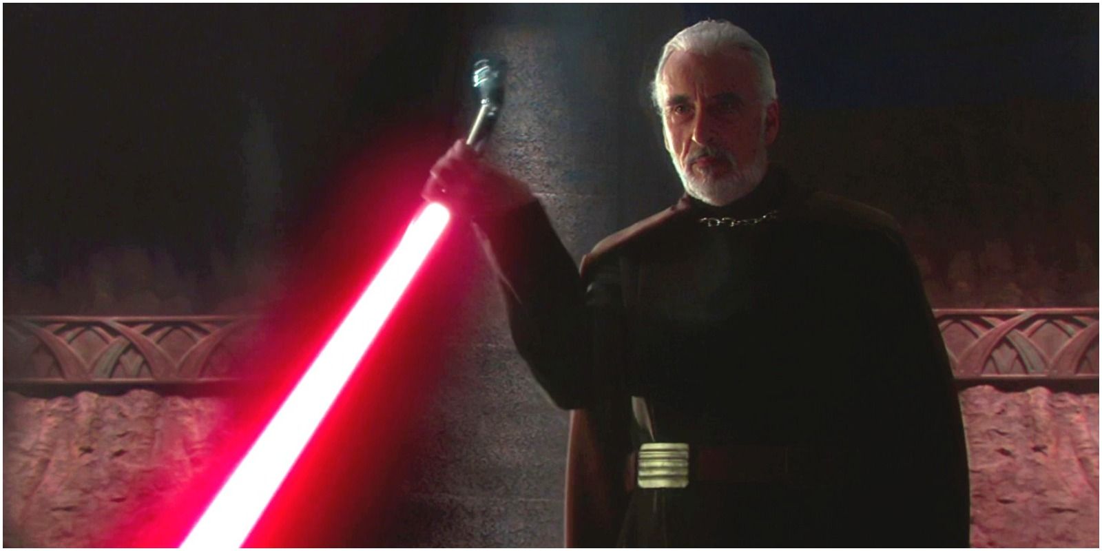 Count Dooku wields a red lightsaber while stood in front of a stone wall