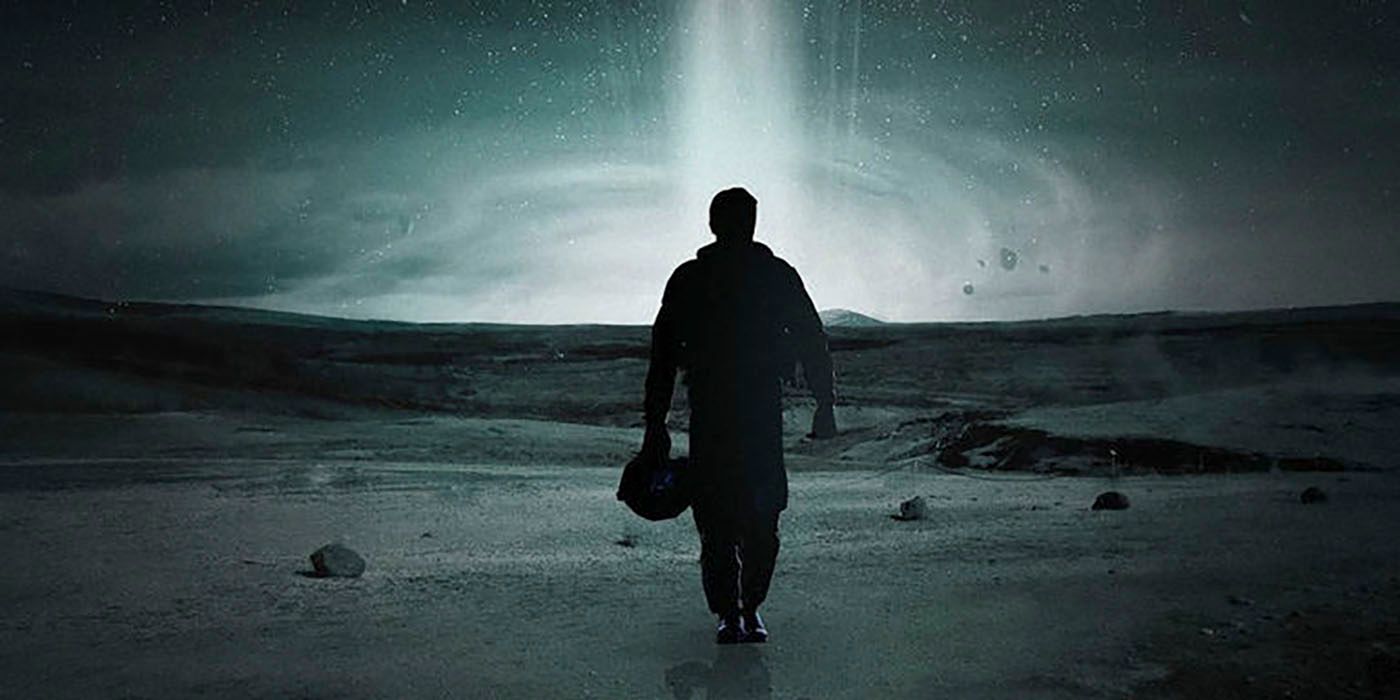 matthew mcconaughey's character walks toward a bright light across a bleak landscape, holding an astronaut helmet in a poster for Interstellar