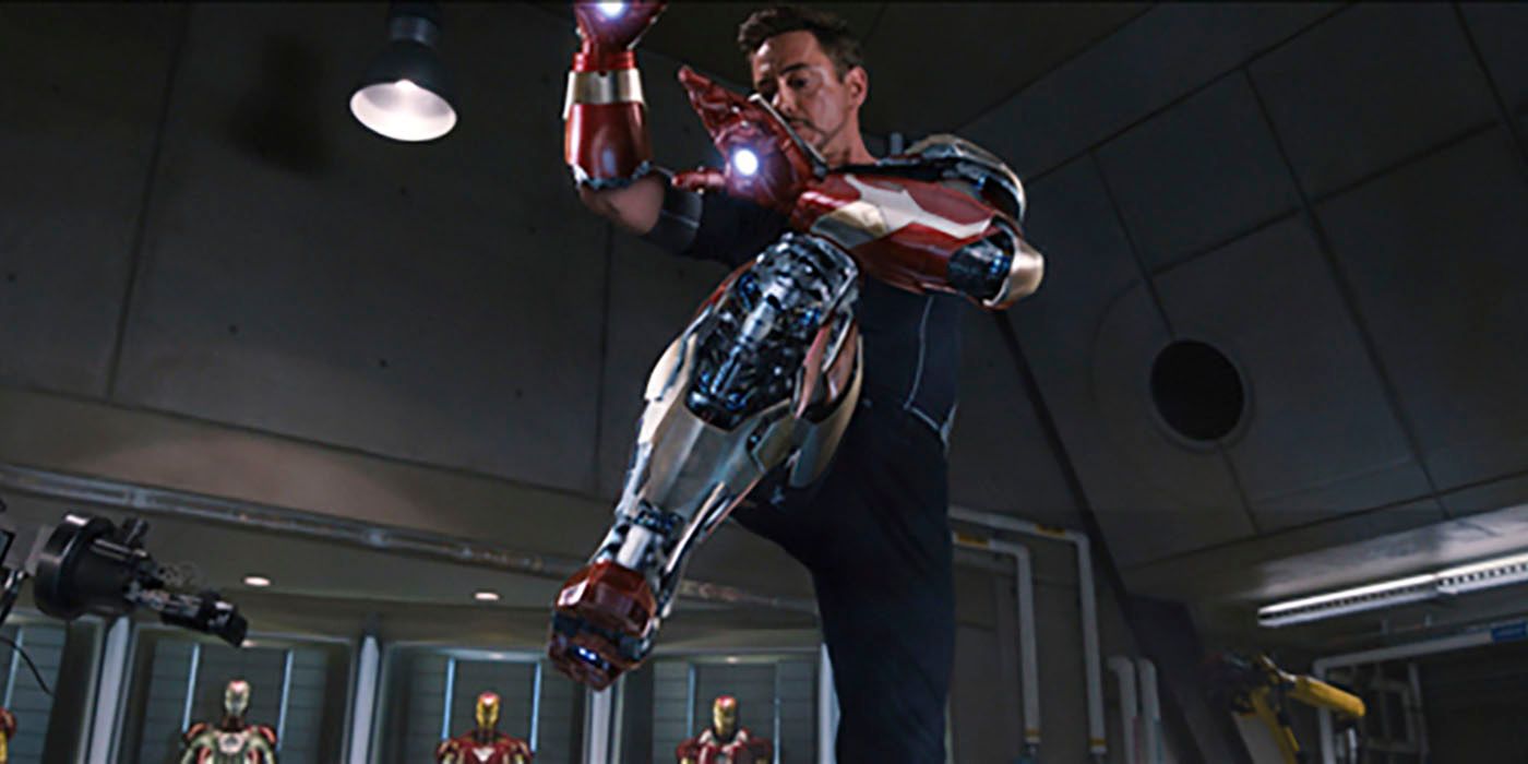 Tony Stark lifts one foot and protects himself with his arms as the pieces of his suit fly toward him to form the Iron Man suit.