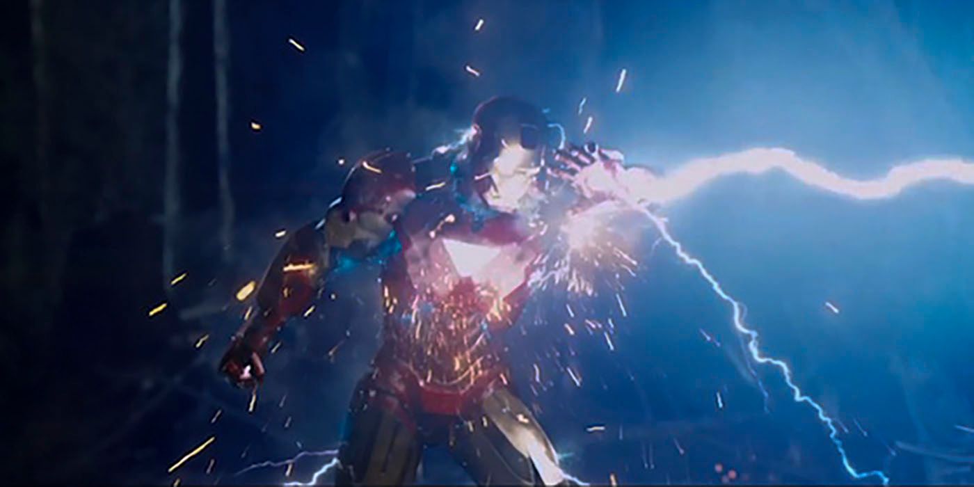 Tony Stark in the iron man armor holds one arm up to protect himself as a bolt of lightning hits the suit