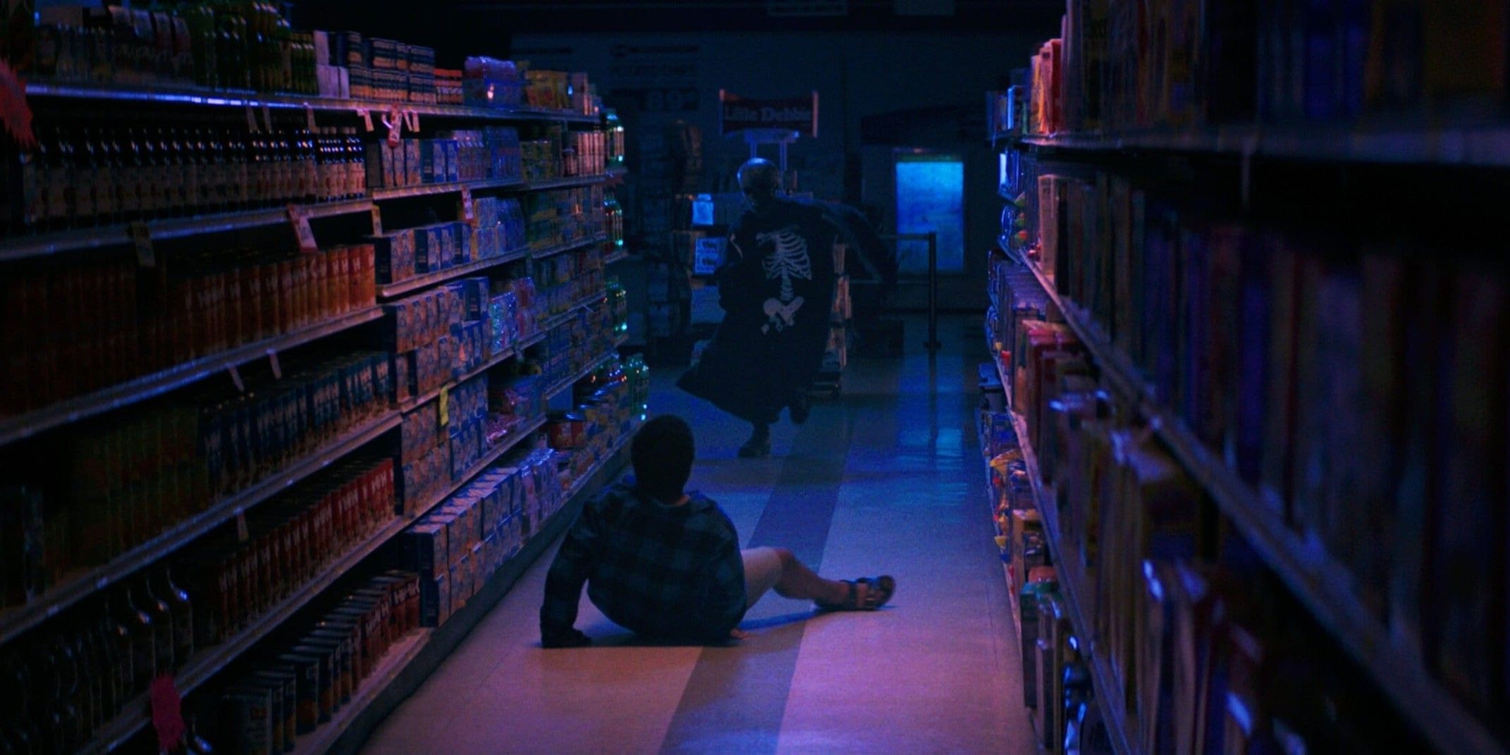 Josh on the floor in a drug store aisle as the skeleton-dressed man runs at him.
