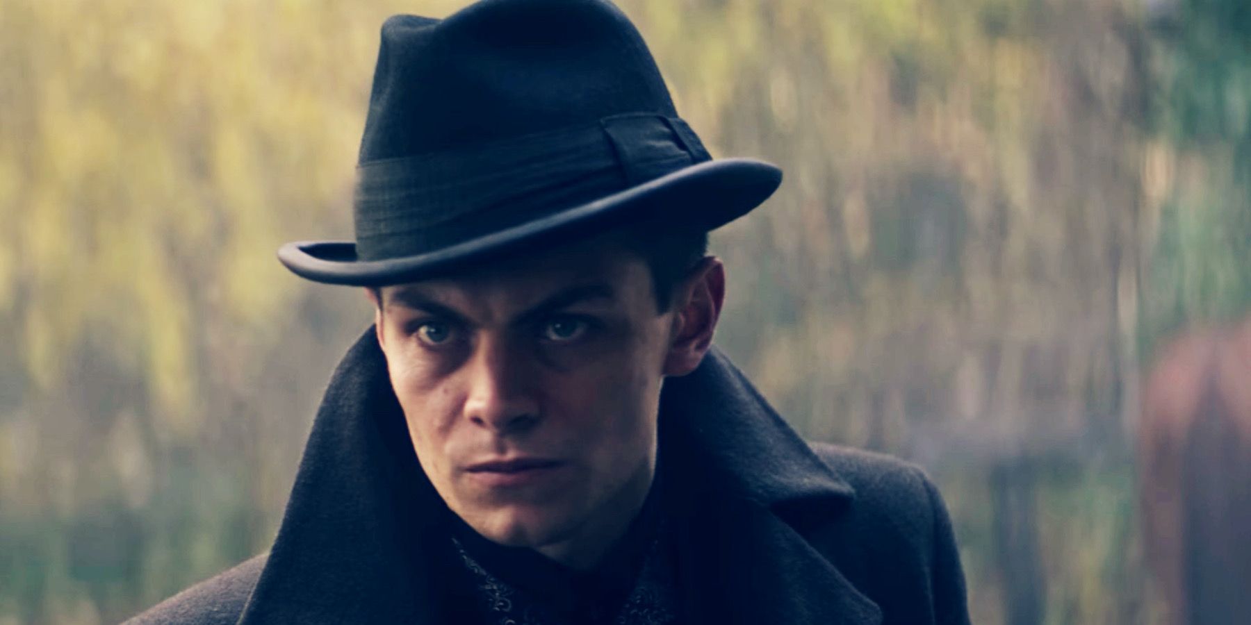 A close-up image of Kaz Brekker, a pale man with piercing blue eyes wearing a coat and a hat.