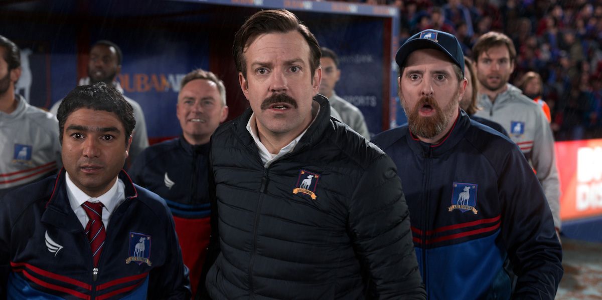 Ted Lasso, Nate and Coach Beard all look shocked in a scene from Ted Lasso.