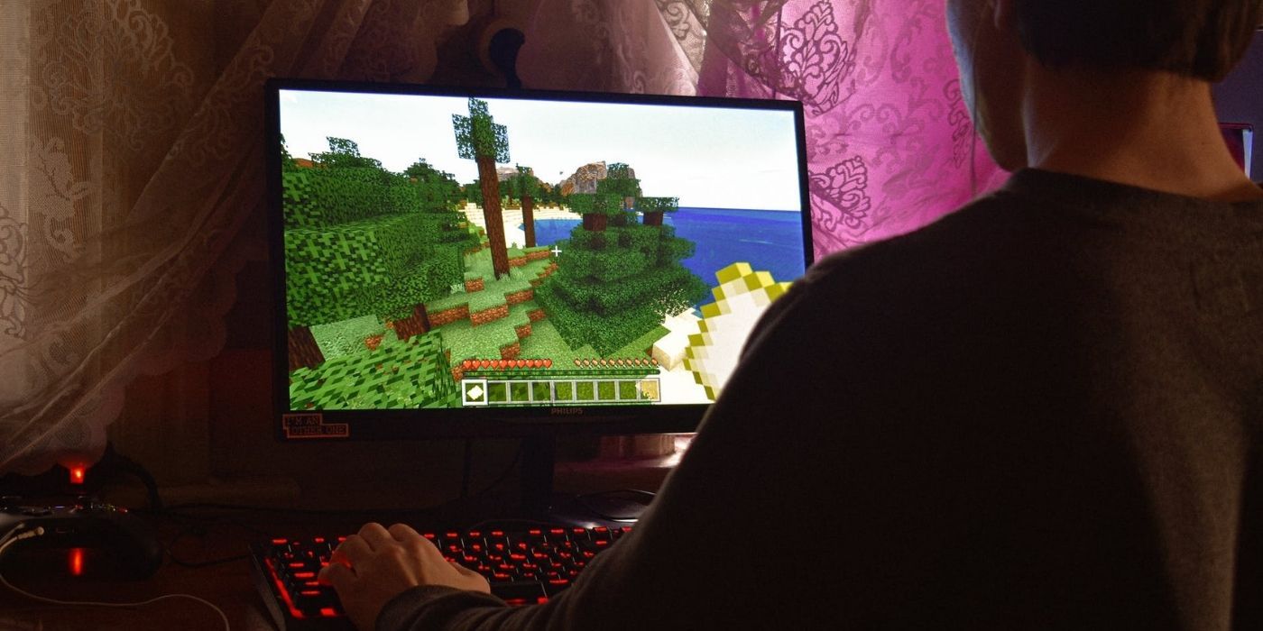 Person sitting in a dimly lit room playing Minecraft on a computer