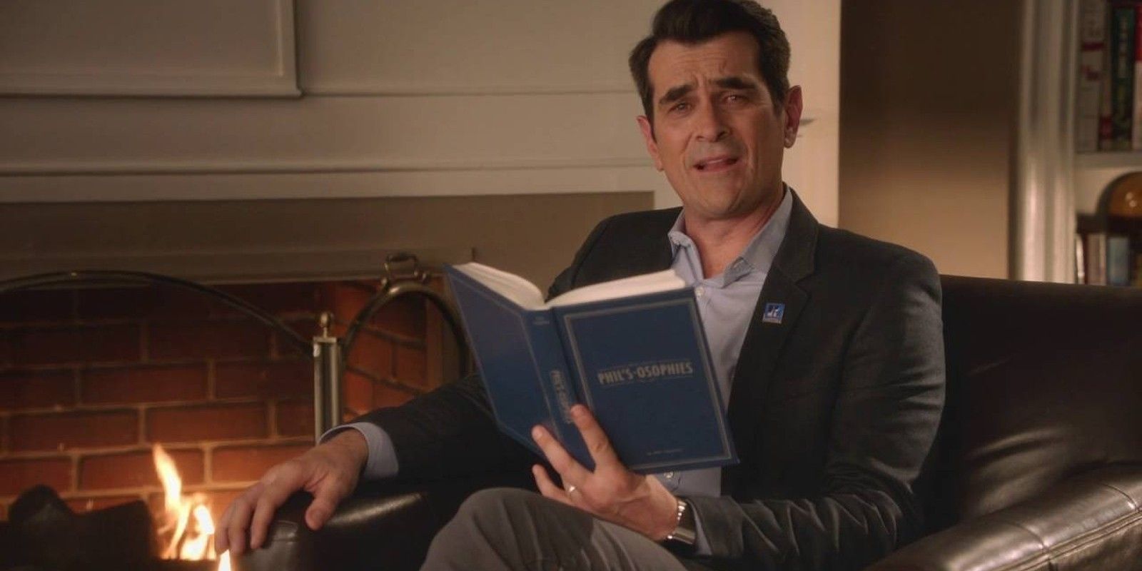 Phil Dunphy from Modern Family sitting on a chair reading a book.