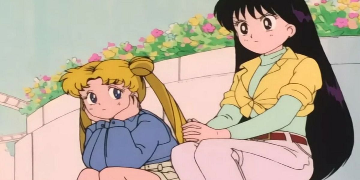 Usagi (Sailor Moon) y Rei (Sailor Mars) se sientan afuera cerca de unas flores. Usagi tiene una expresión ligeramente preocupada en su rostro, mientras que Rei parece decidida.