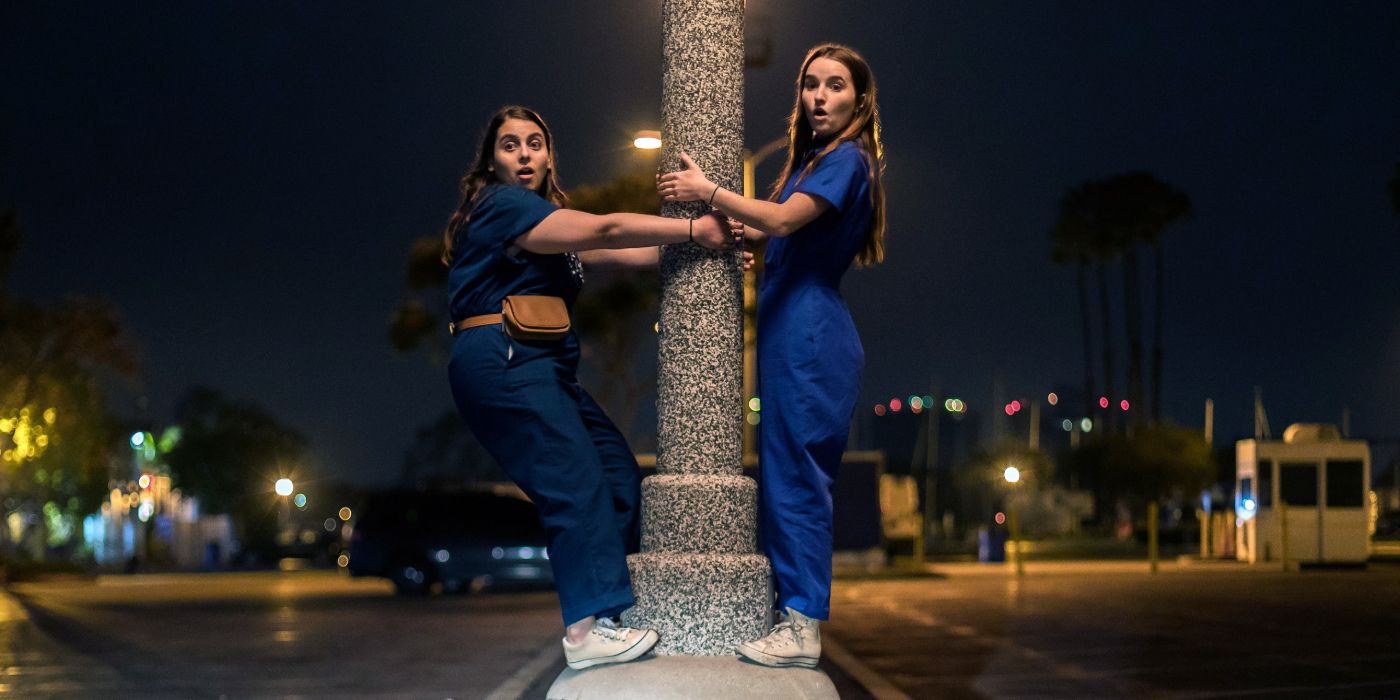Beanie Feldstein and Kaitlyn Dever stand on top of a pole in the street in Booksmart