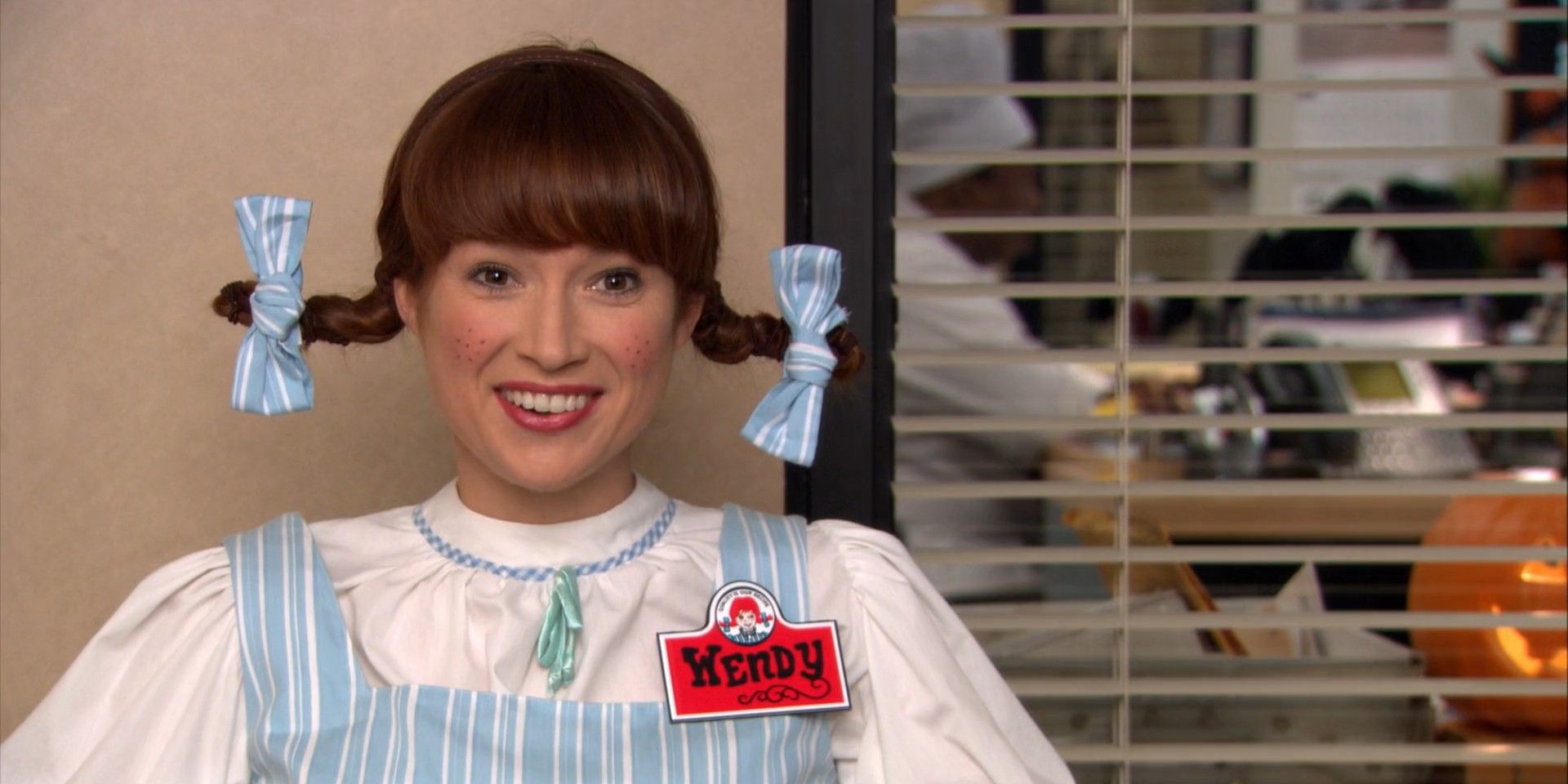 Erin, played by Ellie Kemper, smiling and dressed as Wendy in The Office