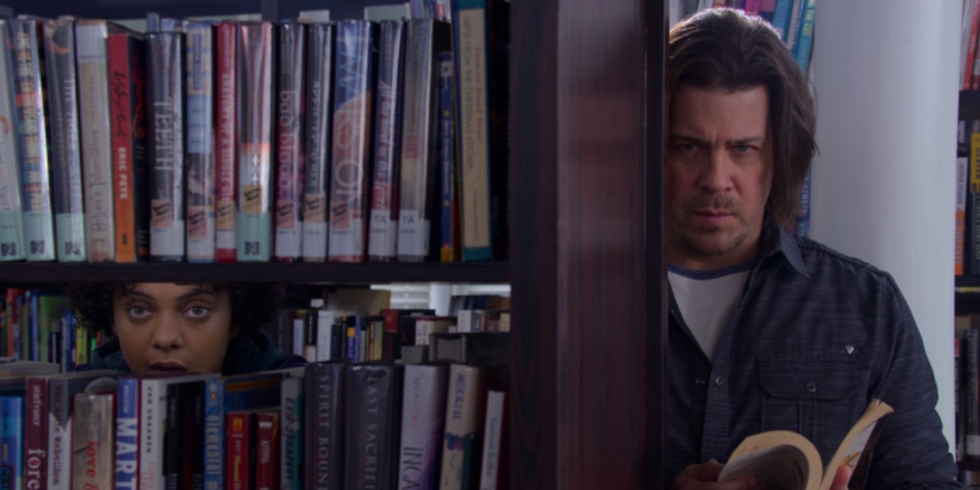 Eliot stands by a book shelf reading in Leverage: Redemption