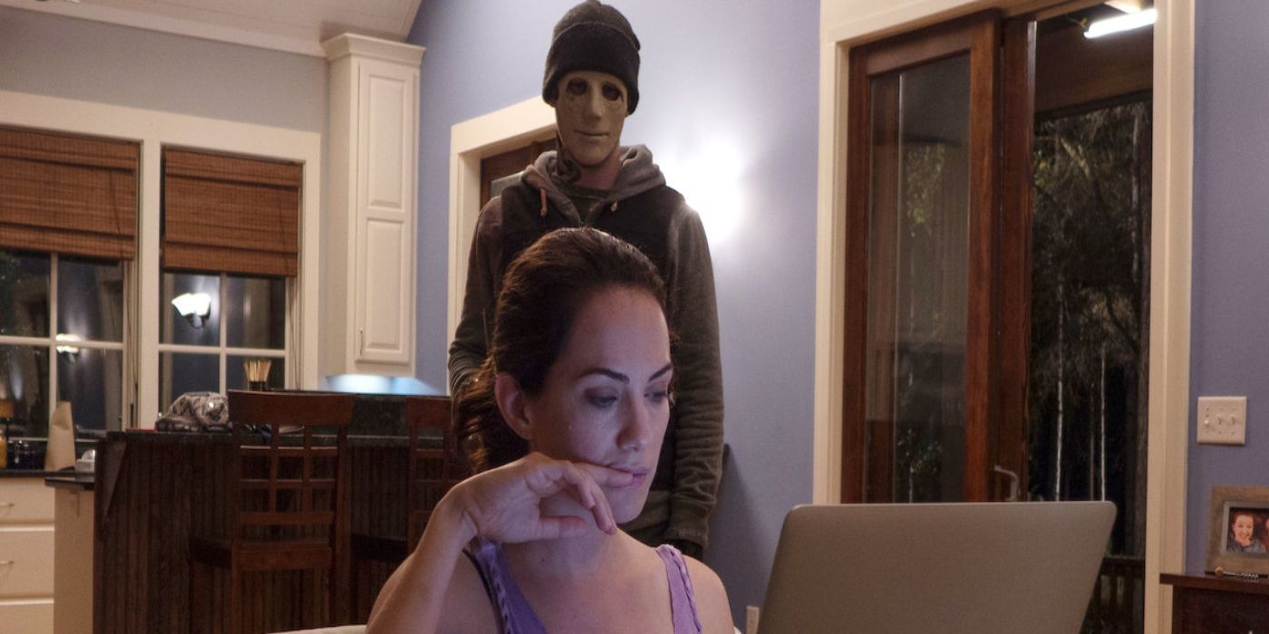 the main character sitting at her laptop while a robber is behind her in Hush