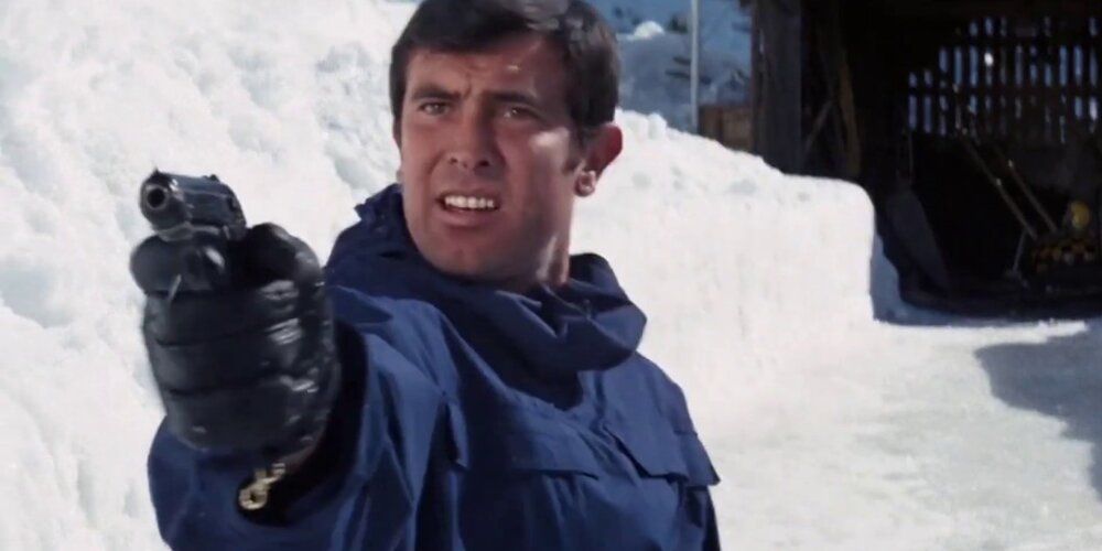 George Lazenby dans le rôle de James Bond pointant une arme dans la neige dans Au service secret de Sa Majesté