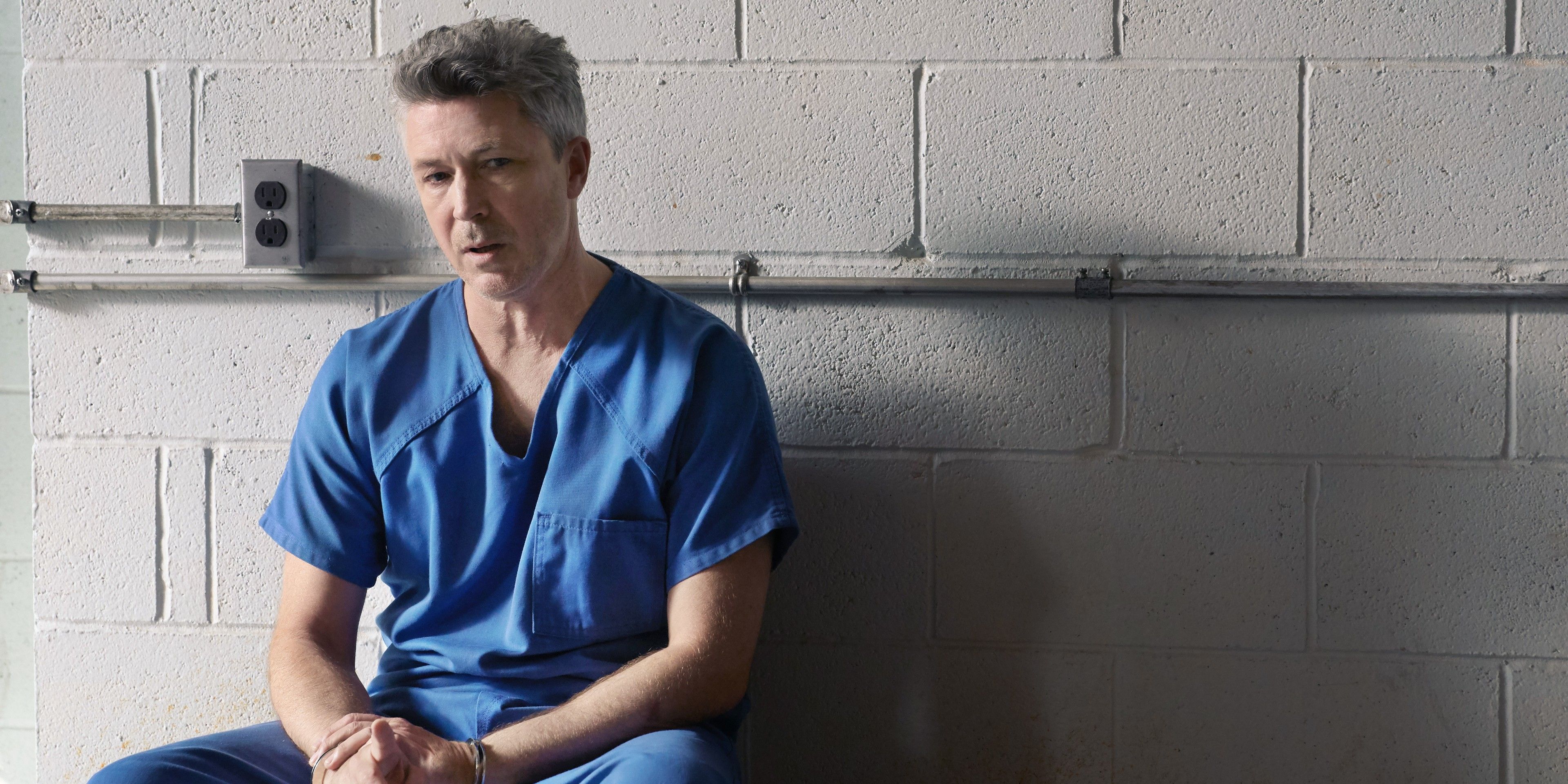 Gillen, handcuffed, sits against a cement wall