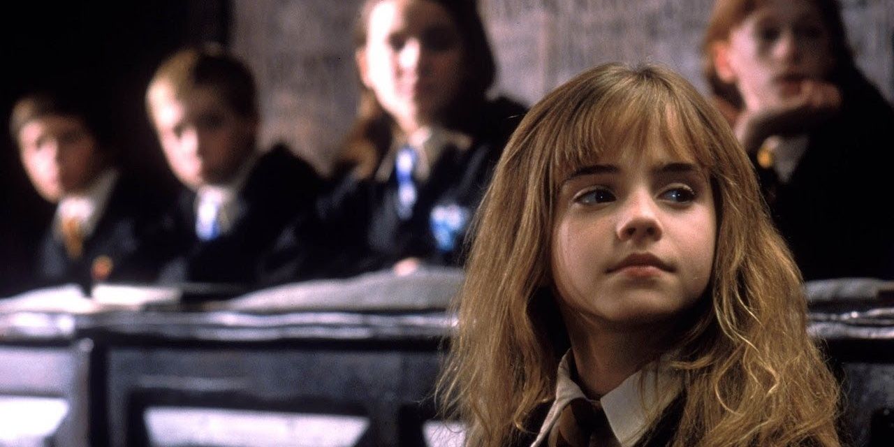 Hermione sits by her desk while attentively listening to a Hogwarts teacher