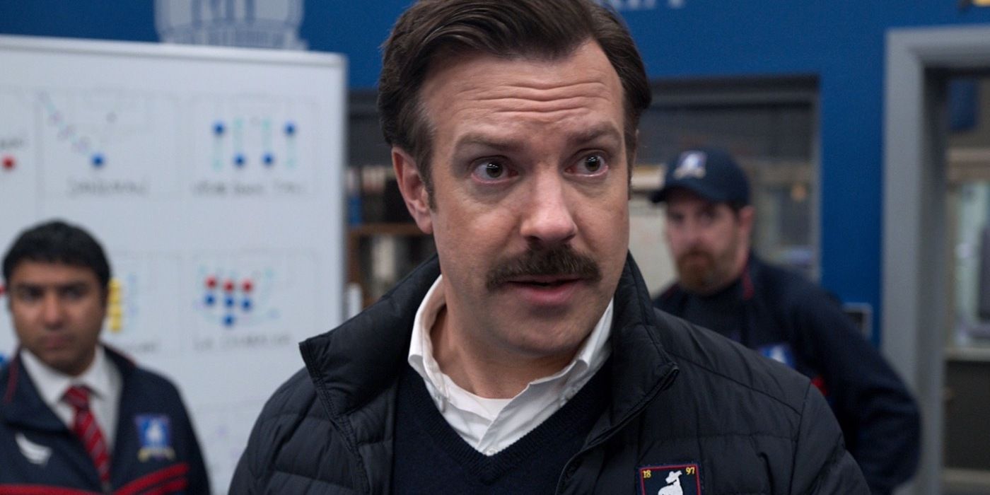 Jason Sudeikis as Coach Ted Lasso standing in front of a play board in the locker room.