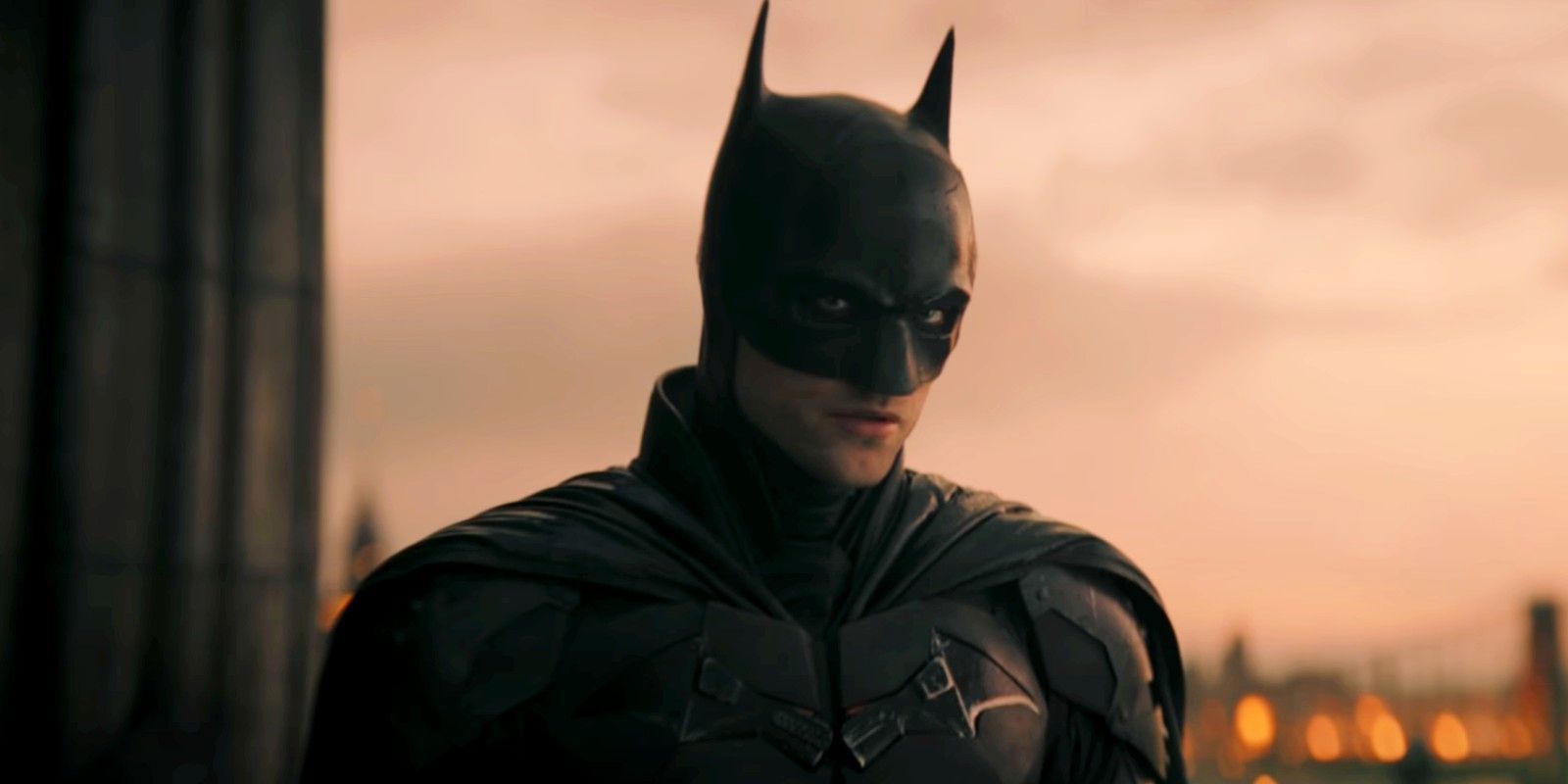 Robert Pattinson as Batman standing on a roof in The Batman