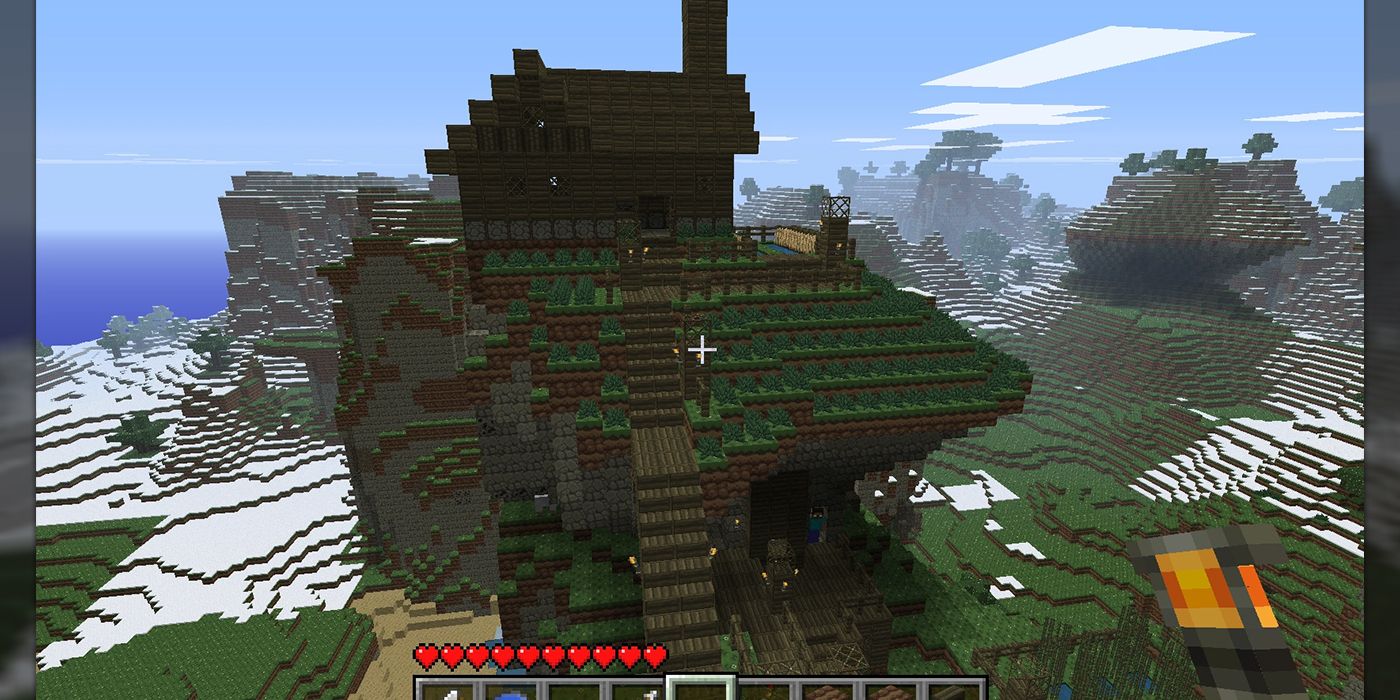 A Minecraft house with Herobrine hidden in the shadows below a cliff.