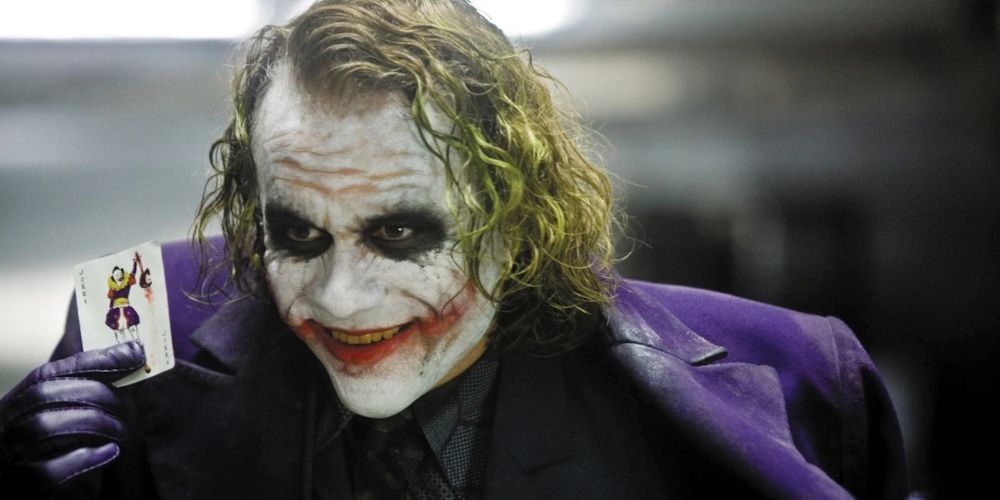 Heath Ledger's Joker holds a playing card while smiling