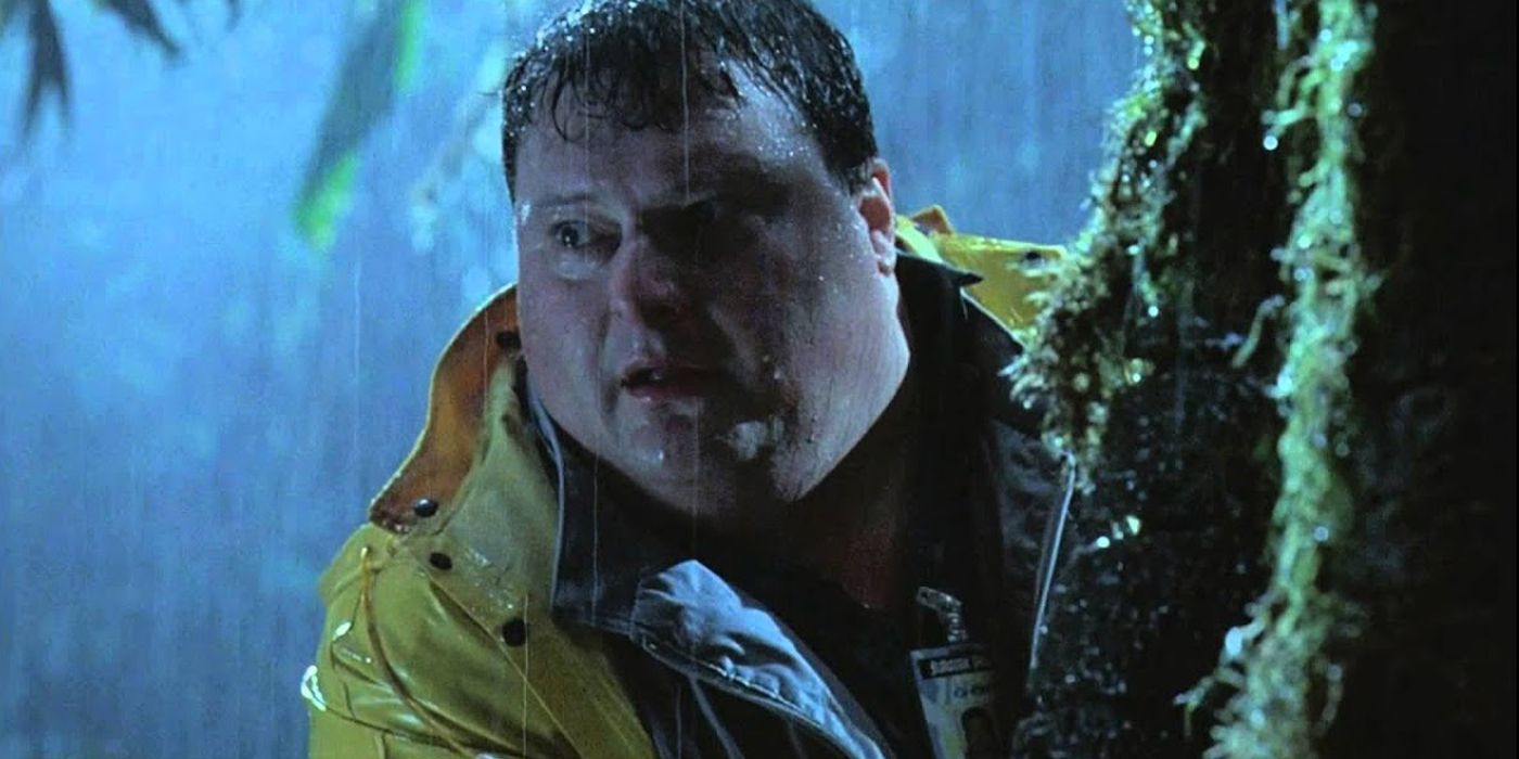 Dennis Nedry hides behind a tree and cautiously looks off in the distance in Jurassic Park