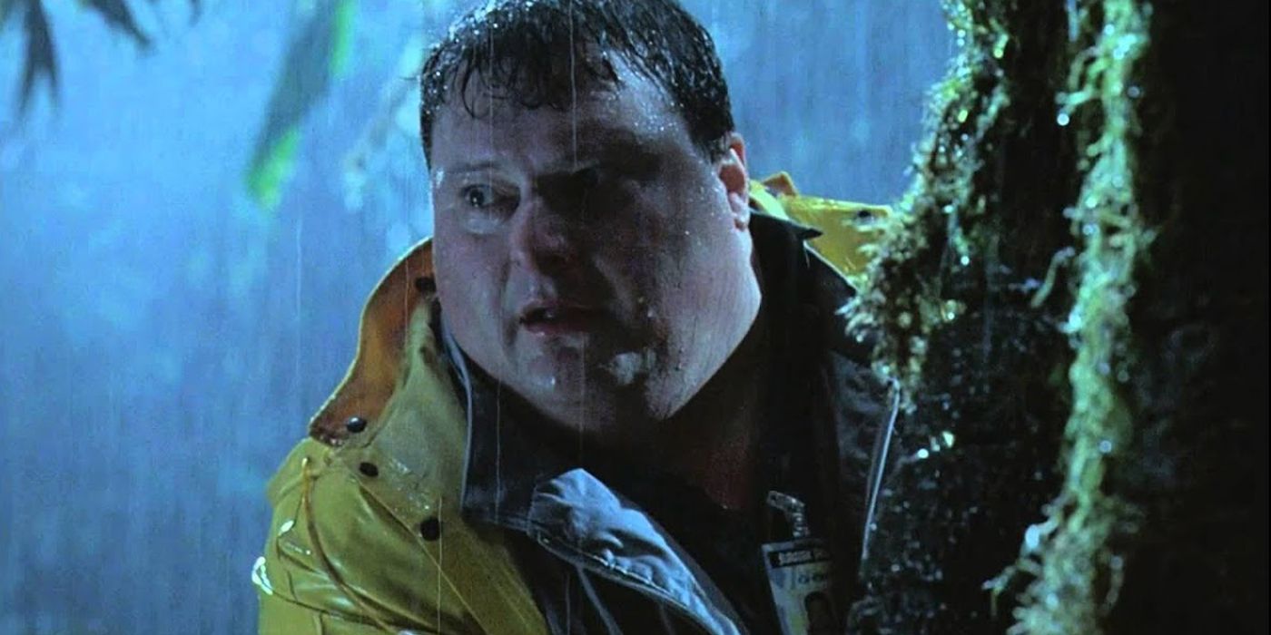 Dennis Nedry se esconde atrás de uma árvore e olha cautelosamente para longe em Jurassic Park