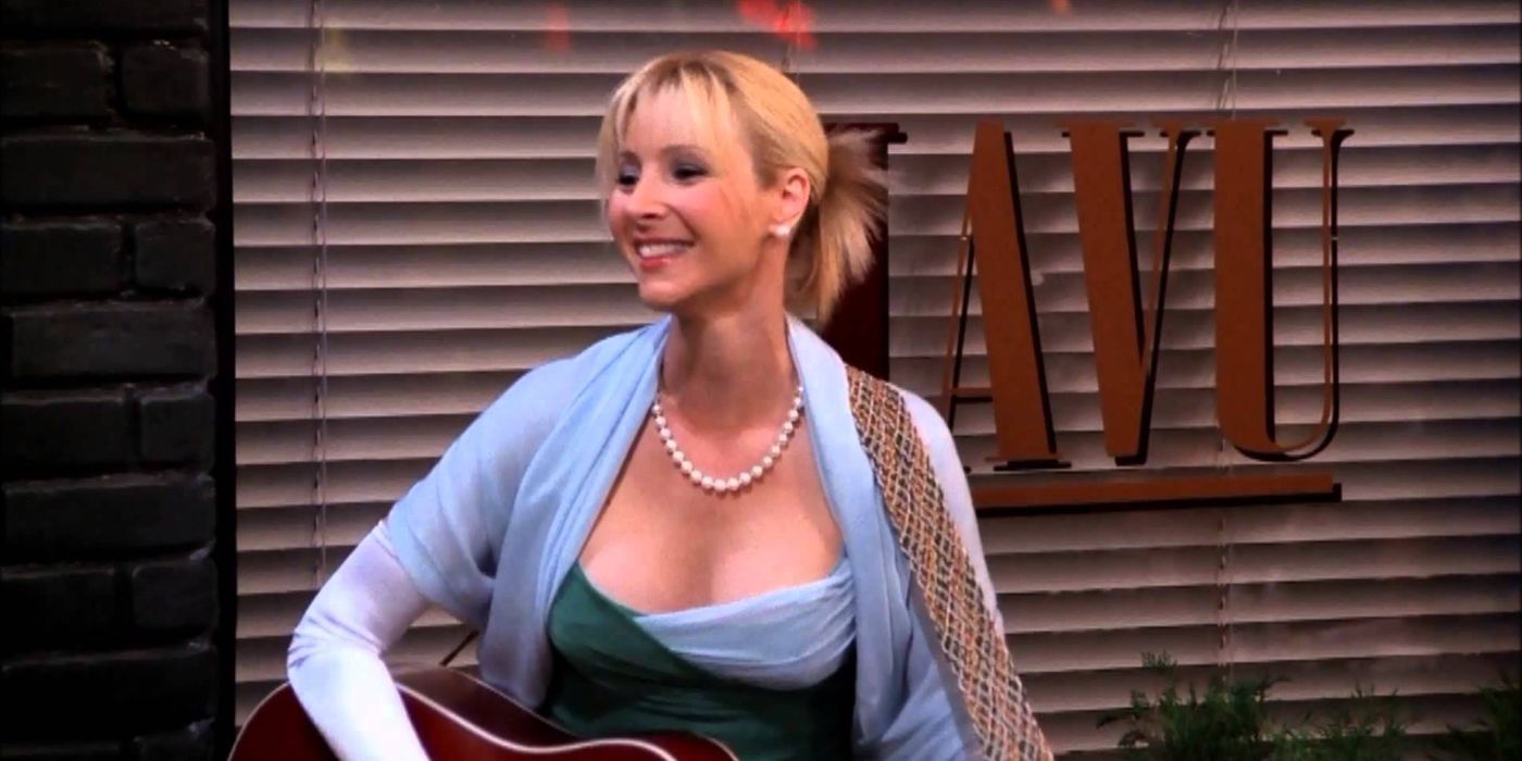 Phoebe Buffay smiles while holding her guitar outside a storefront in Friends