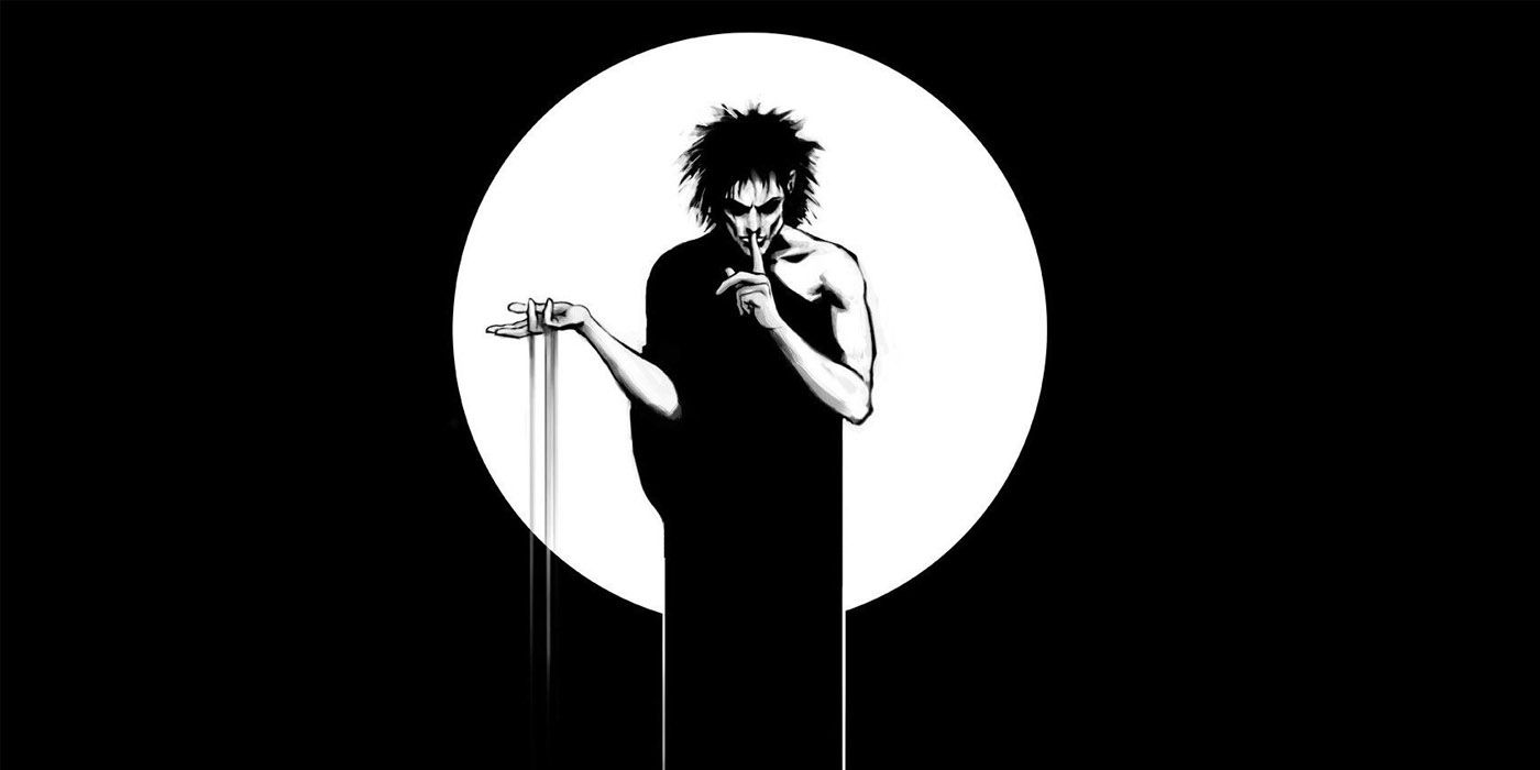 A pale man stands in front of a white circle in a black background, holds his finger to his lips while sand falls from his other hand
