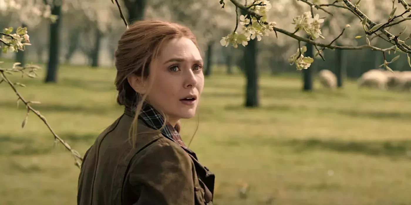 Wanda wearing a brown jacket and with her hair tied up, standing in an orchard of apple blossoms.