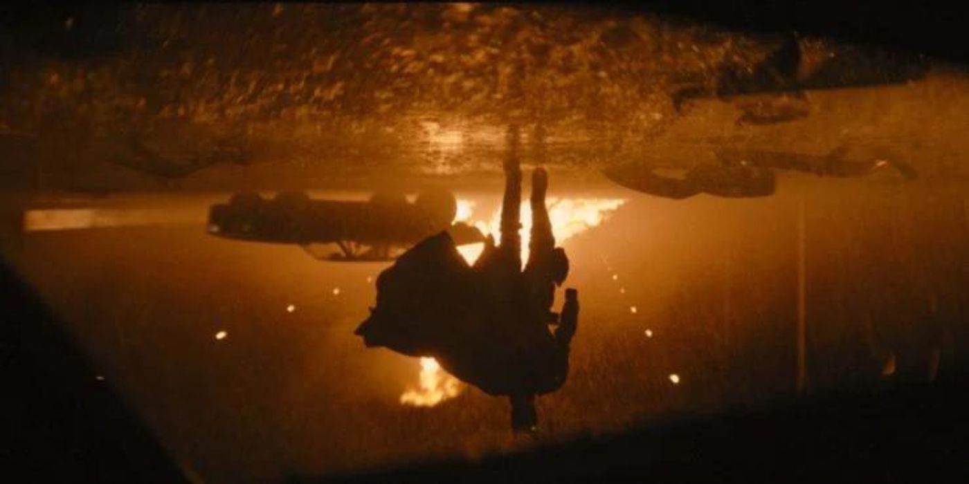 In a still from The Batman (2022), Batman walks toward the camera as fire erupts behind him.