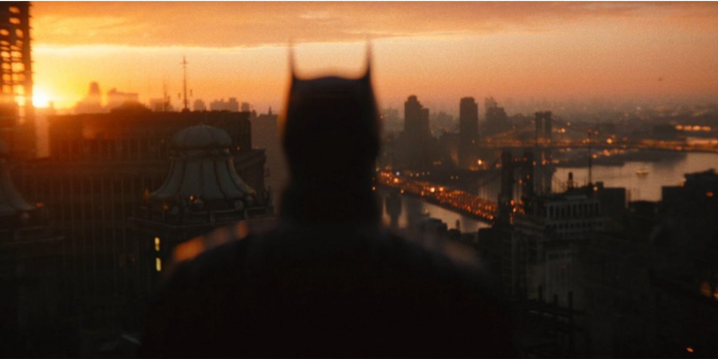In a still from The Batman (2022), Batman watches over Gotham City as the sun sets.