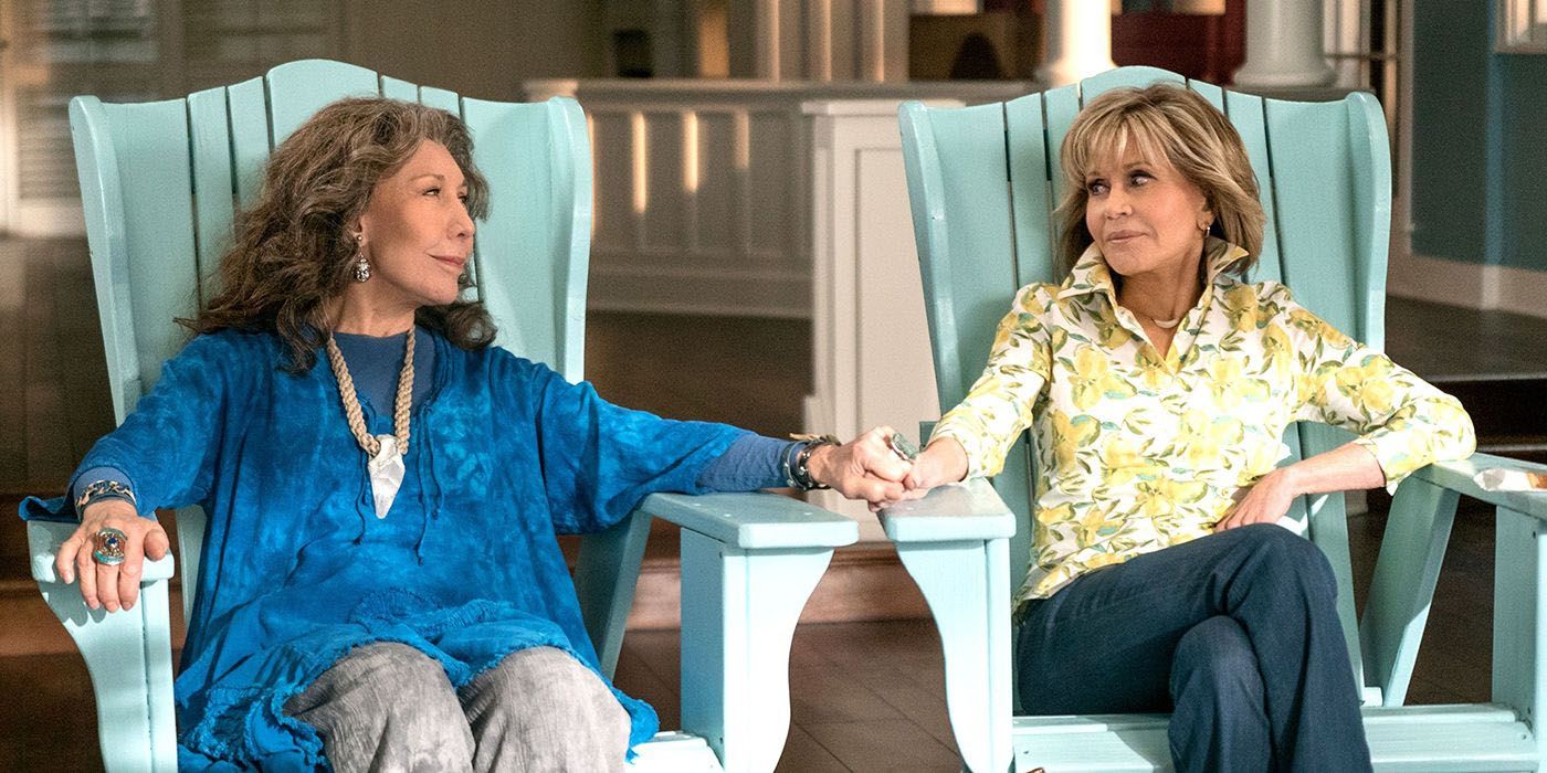 Grace and Frankie relaxing in beach chairs while holding hands.