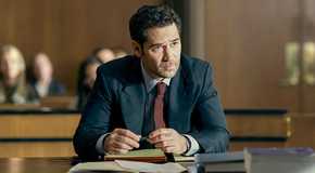 Mickey Haller wears a black suit and leans forward at a court table in The Lincoln Lawyer Season 1