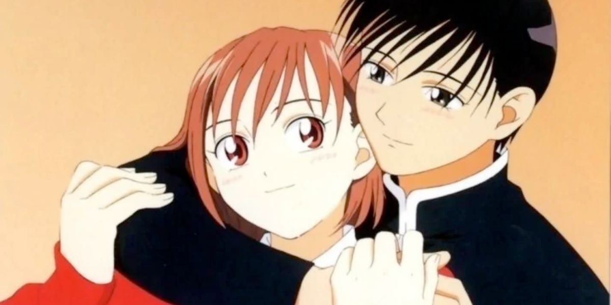 Image features a visual from His and Her Circumstances: (From left to right) Yukino Miyazawa (short, brown hair and wearing a long-sleeved red shirt) is embraced by Soichiro Arima (short, black hair and black hair)