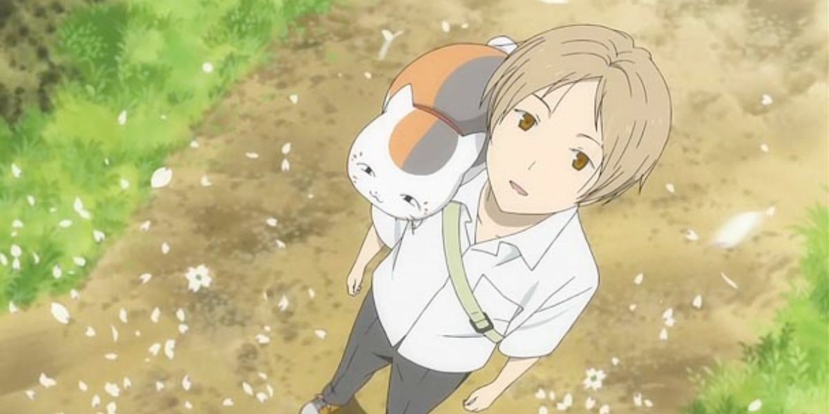 Image features a visual from Natsume's Book of Friends: (From left to right) Nyanko-sensei, or Madara, (plump, white, brown and orange cat) is sitting on Takeshi Natsume (short, brown hair and white shirt, black pants)'s shoulder.