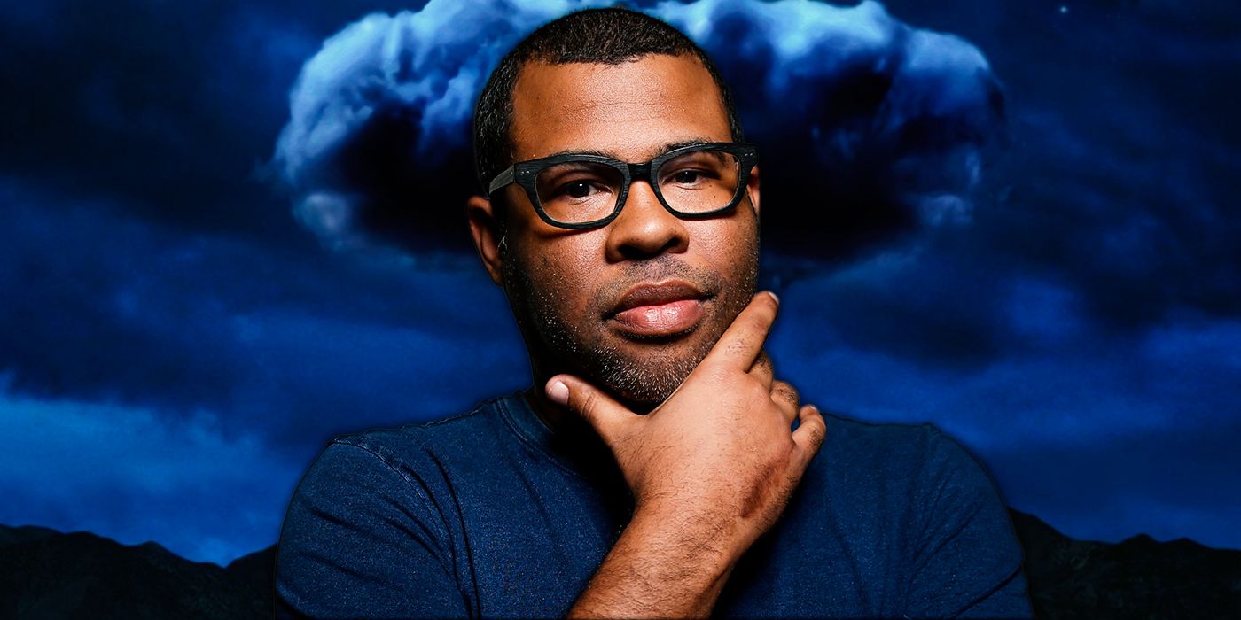 Jordan Peele appearing lost in thought with the poster for Nope behind him