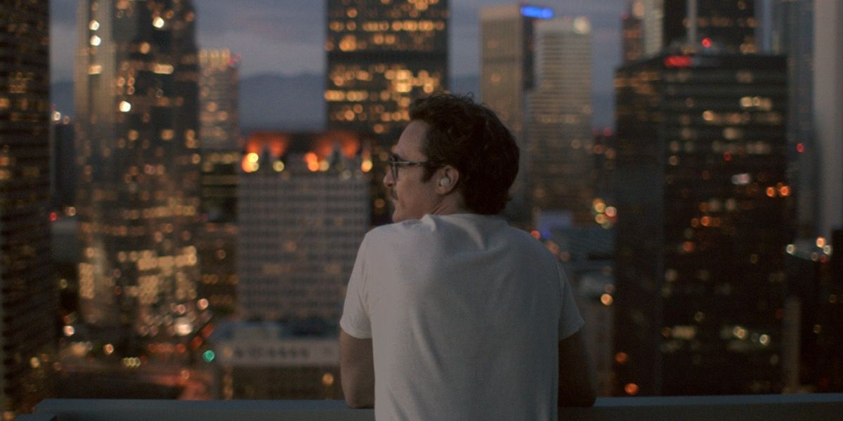 Joaquin Phoenix stands on a balcony looking out at the city in Her