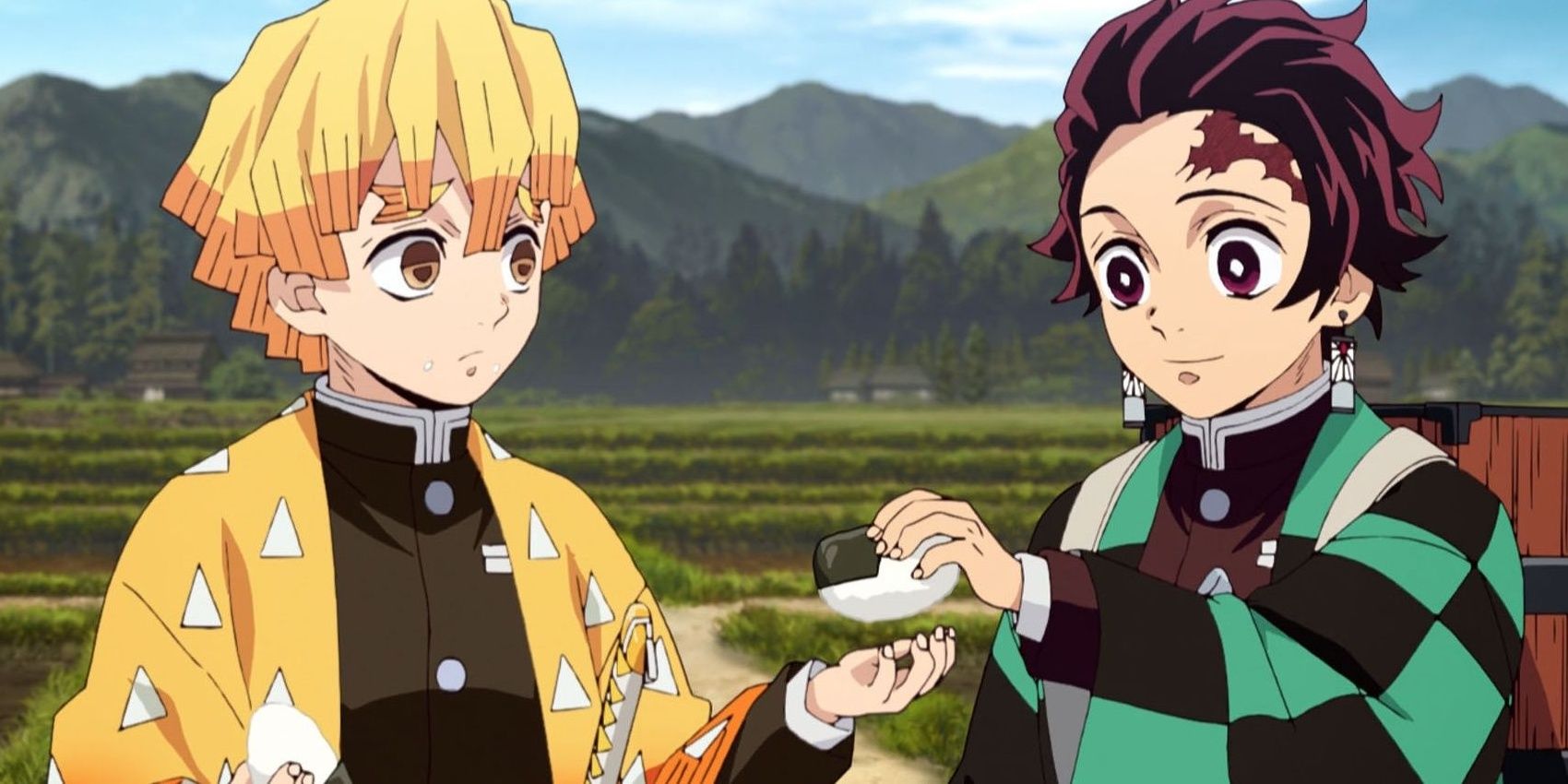 Tanjiro giving Zenitsu a rice ball in front of a field and mountains