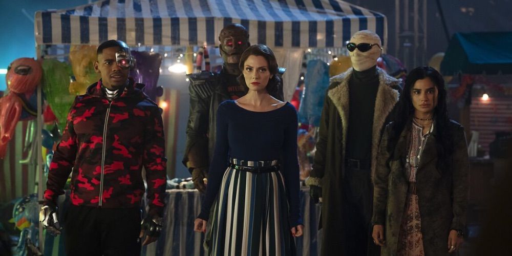 The Doom Patrol team standing together in front of a tent/kiosk