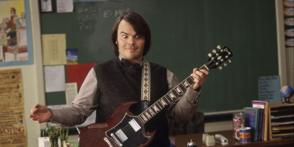 Jack Black as Dewey Finn holding his guitar in front of a classroom in School of Rock